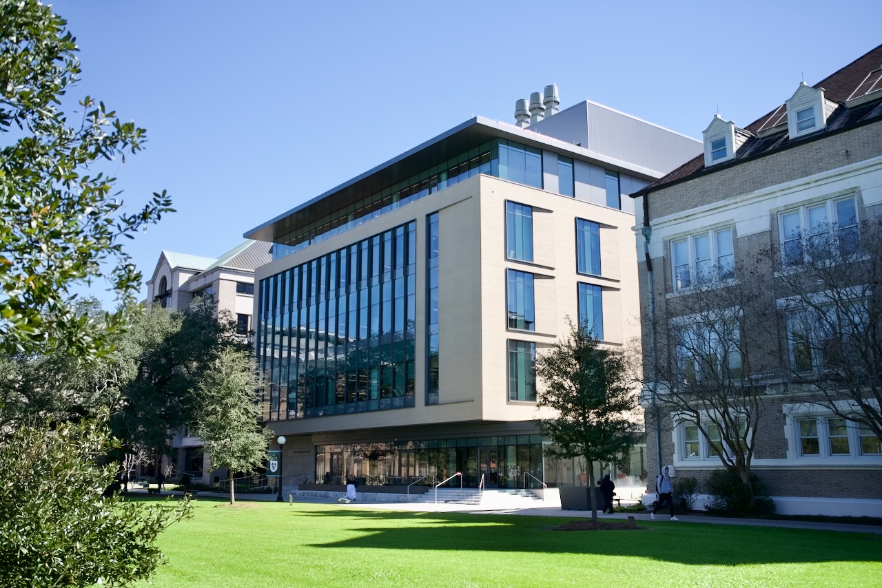 Photograph of a modern glass and concrete building facing a green lawn.