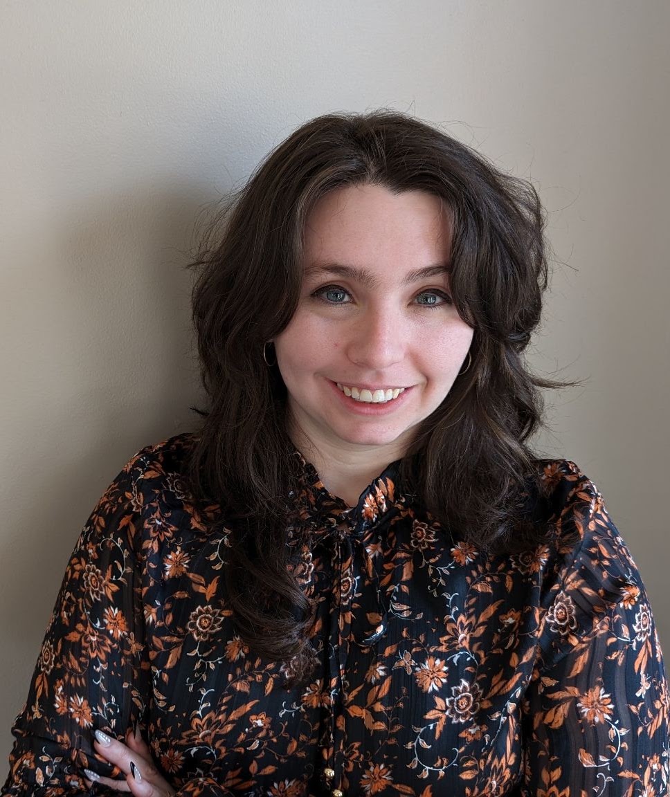 Young woman with dark hair smiling, wearing a floral print blouse.