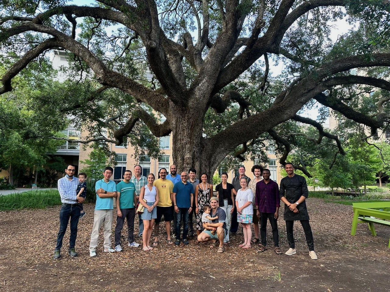 Photograph of a group of adults standing in front of a massive tree with sprawling branches.