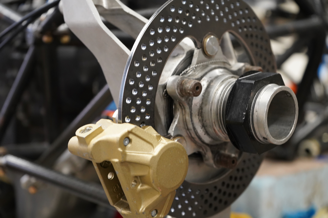 Close-up photograph of a perforated motorcycle brake disc with a gold caliper.