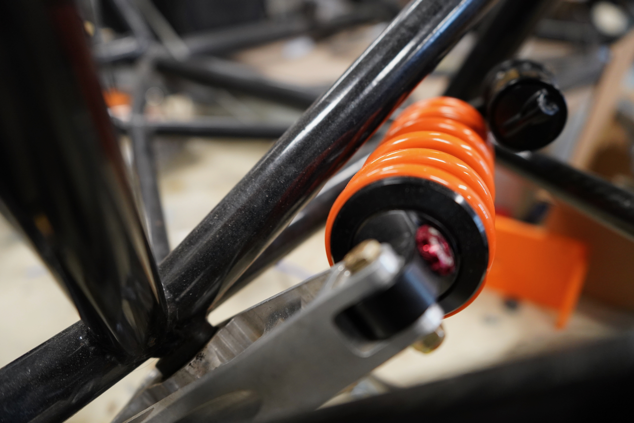 Photograph of an orange coilover shock absorber attached to a vehicle frame.