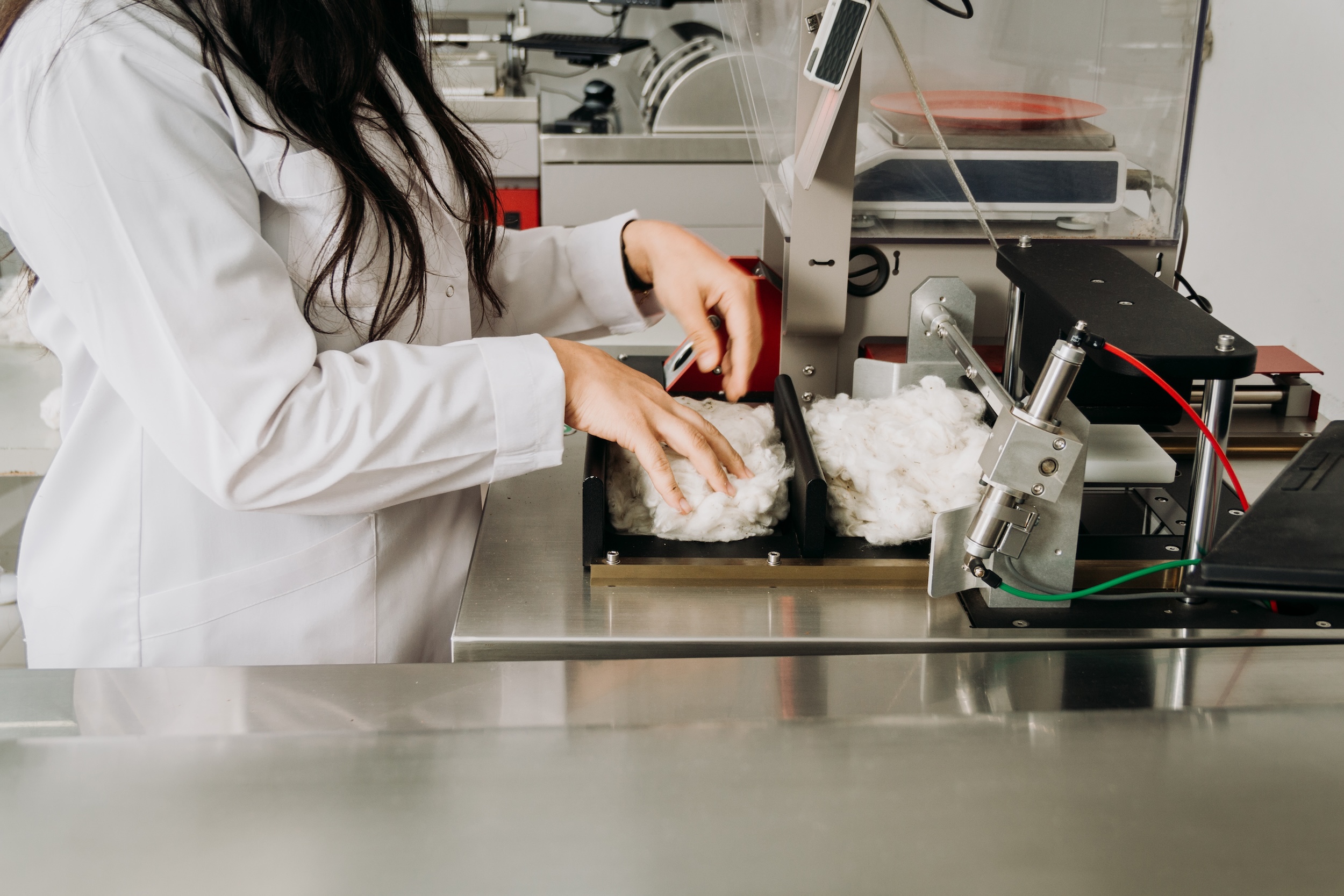Woman in lab coat putting cotton-like material into a machine