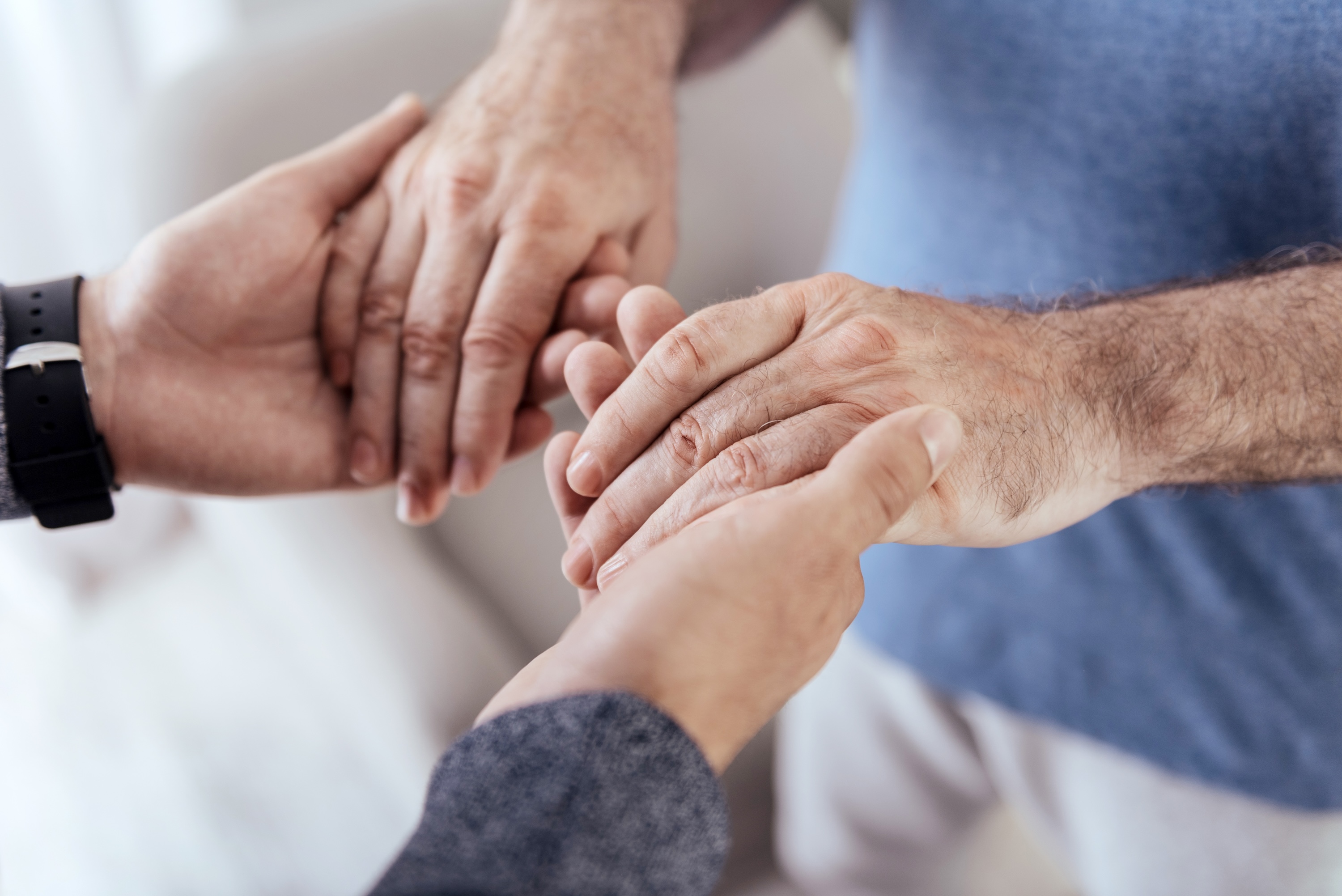 Photograph of a caregiver gently holding an elderly patient's hands.