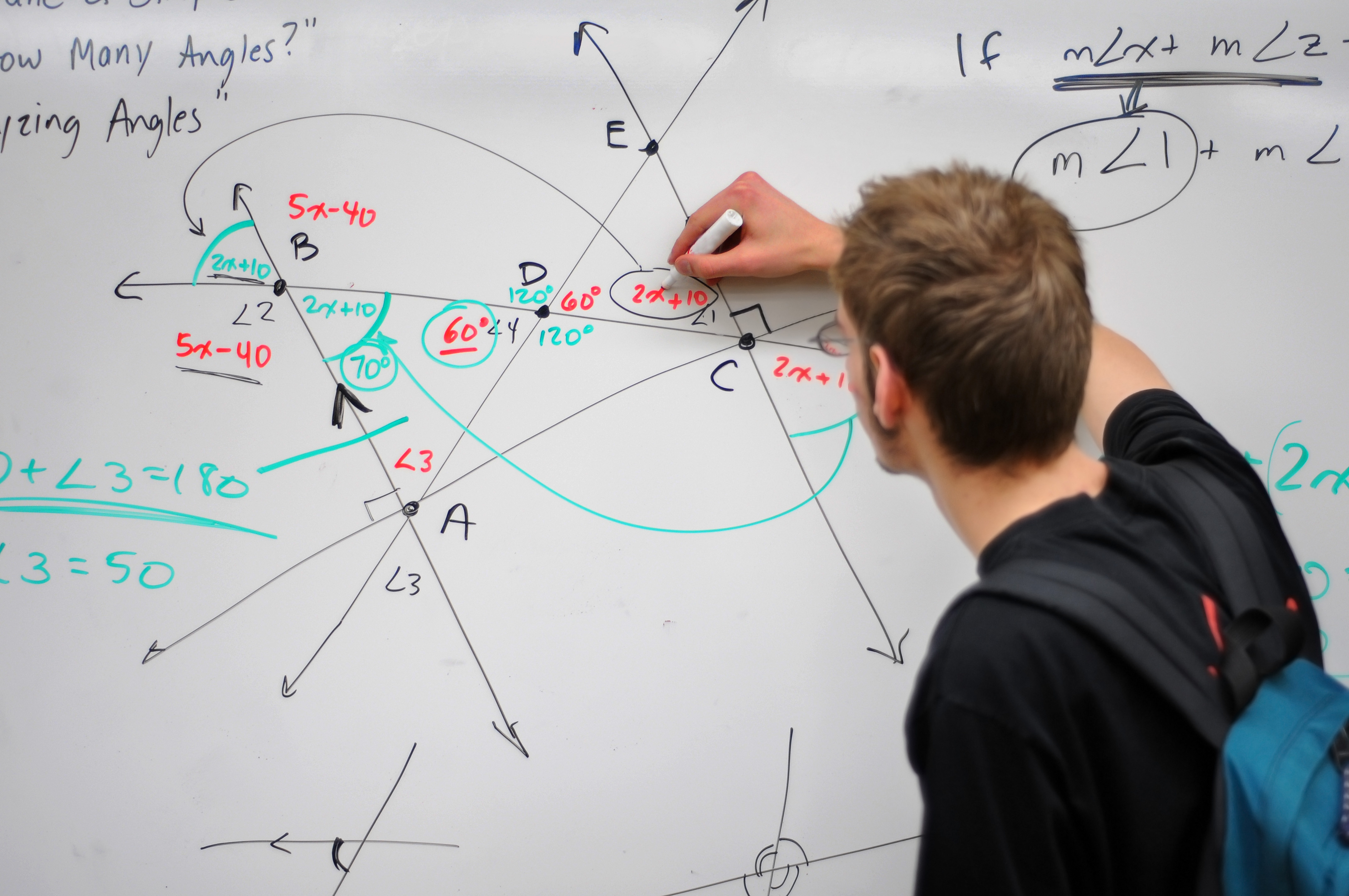 Photograph of a student writing geometric equations and angles on a whiteboard.