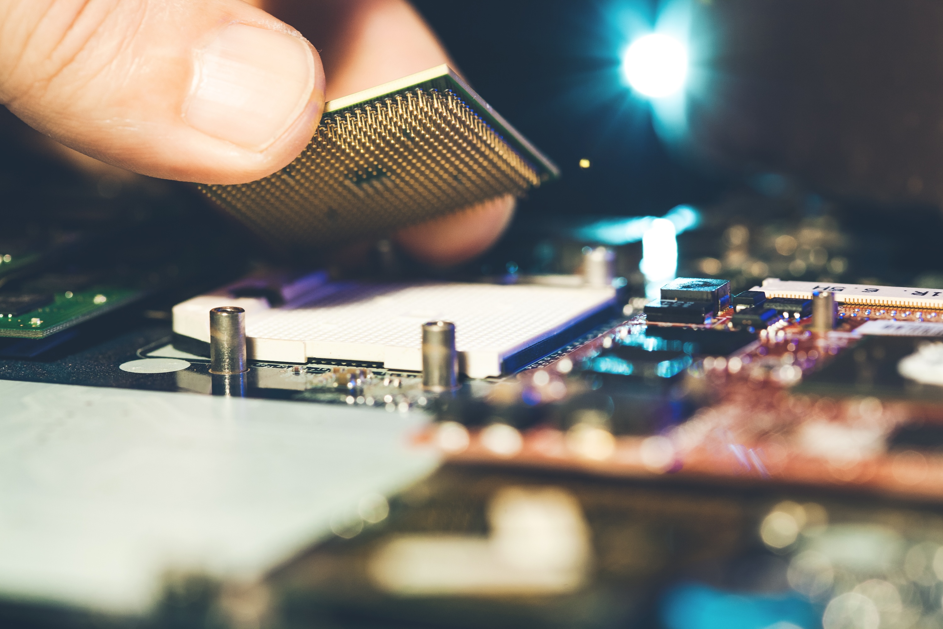 Photograph of a hand installing a CPU chip onto a laptop motherboard.