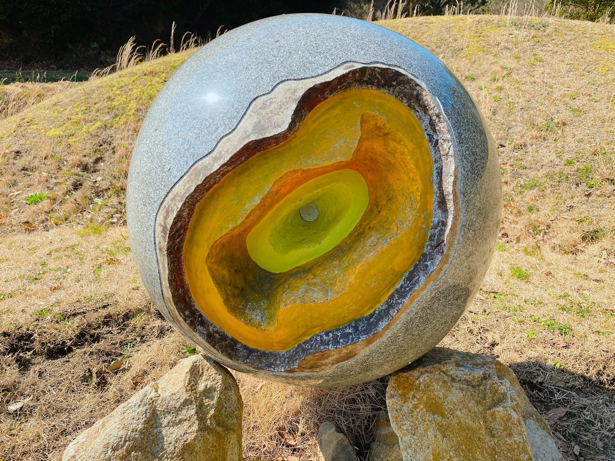 Photograph of a large grey stone sphere with a glowing, layered yellow and orange geode center.