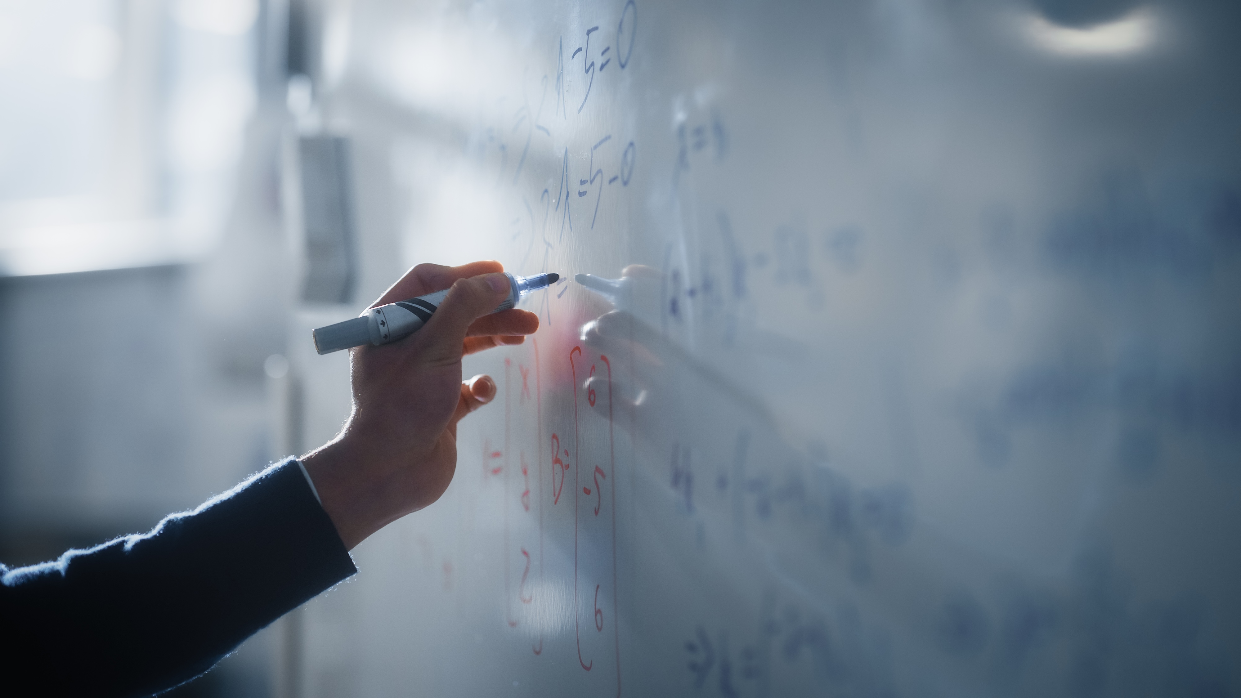 A hand writing mathematical equations on a white board with a marker.
