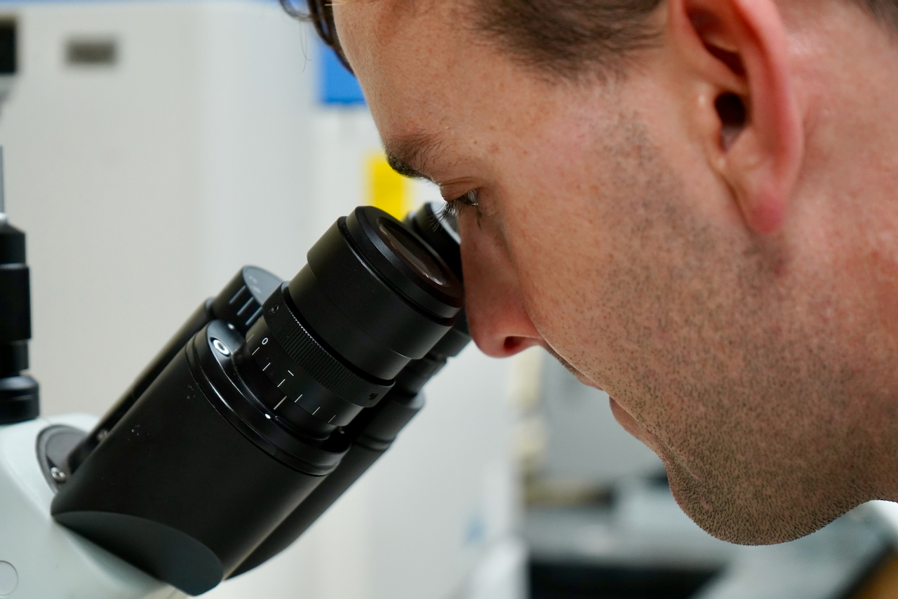 A close-up photograph of a scientist looking through a microscope.