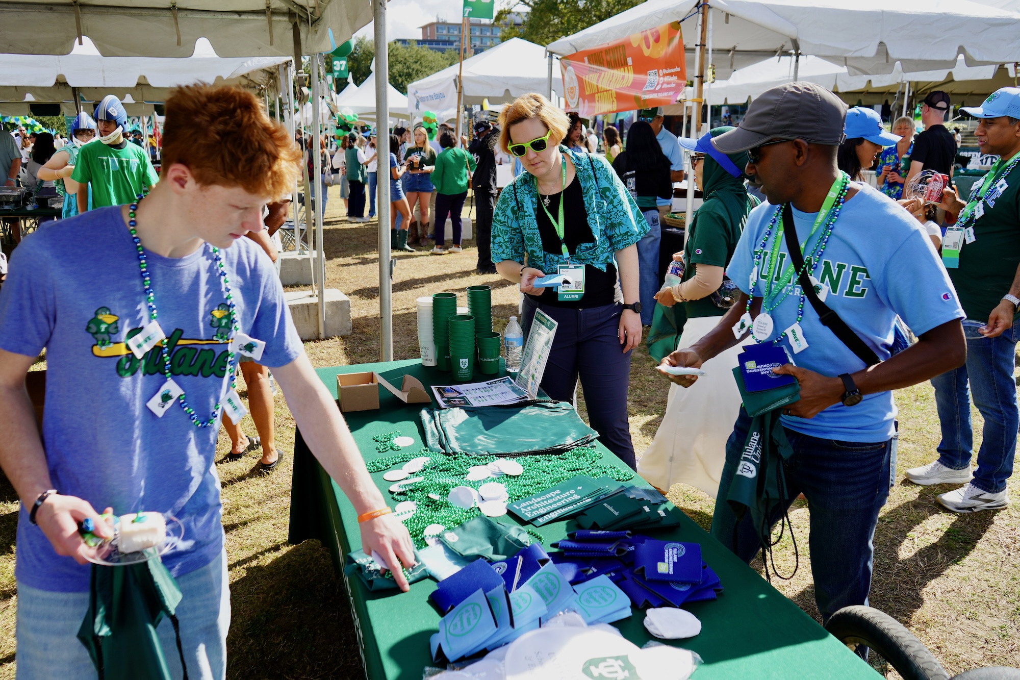 Photograph of people gathering at an outdoor event booth, looking at merchandise.