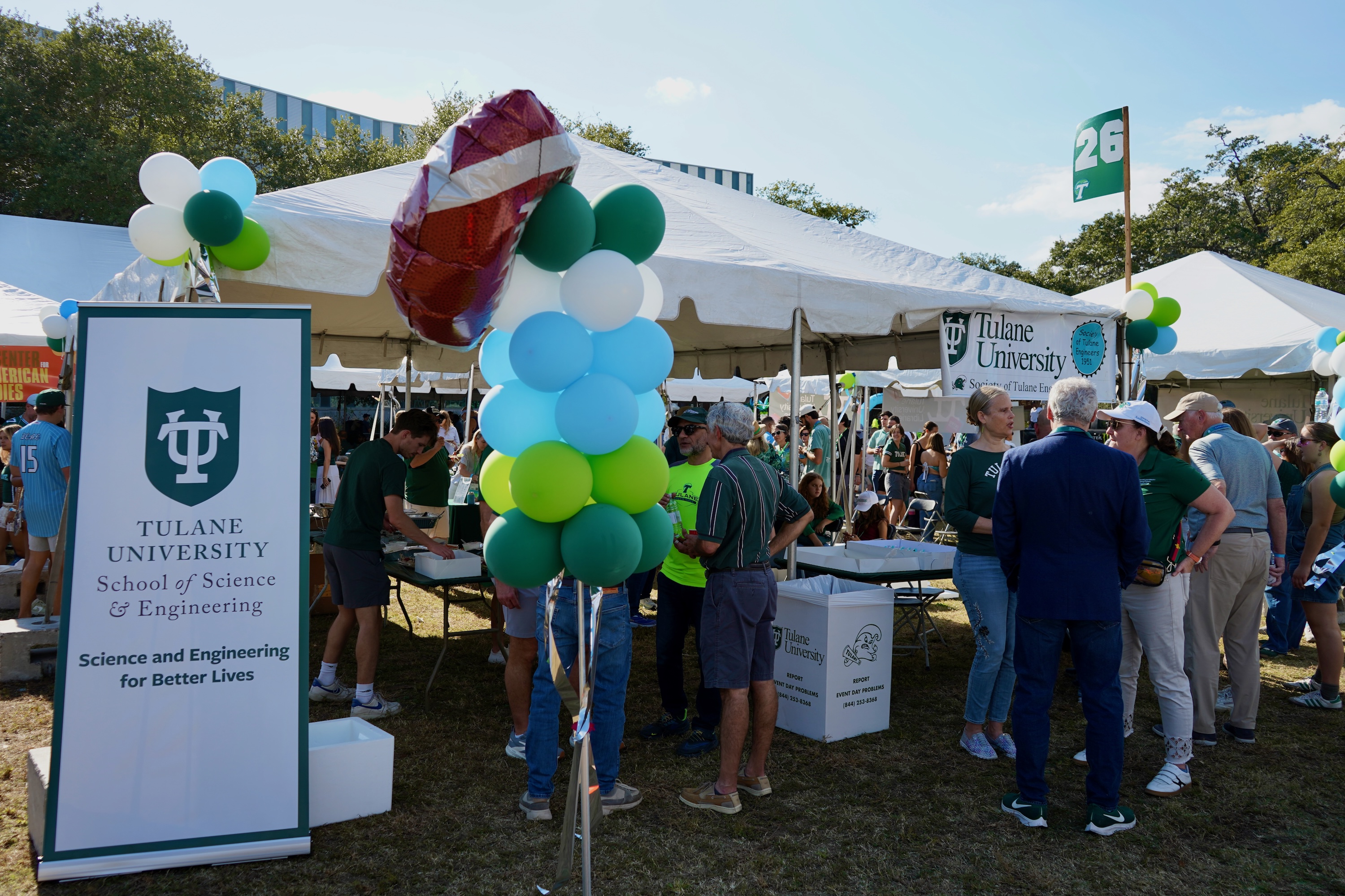Tulane University tent setup with balloons and crowds outside on a sunny day.