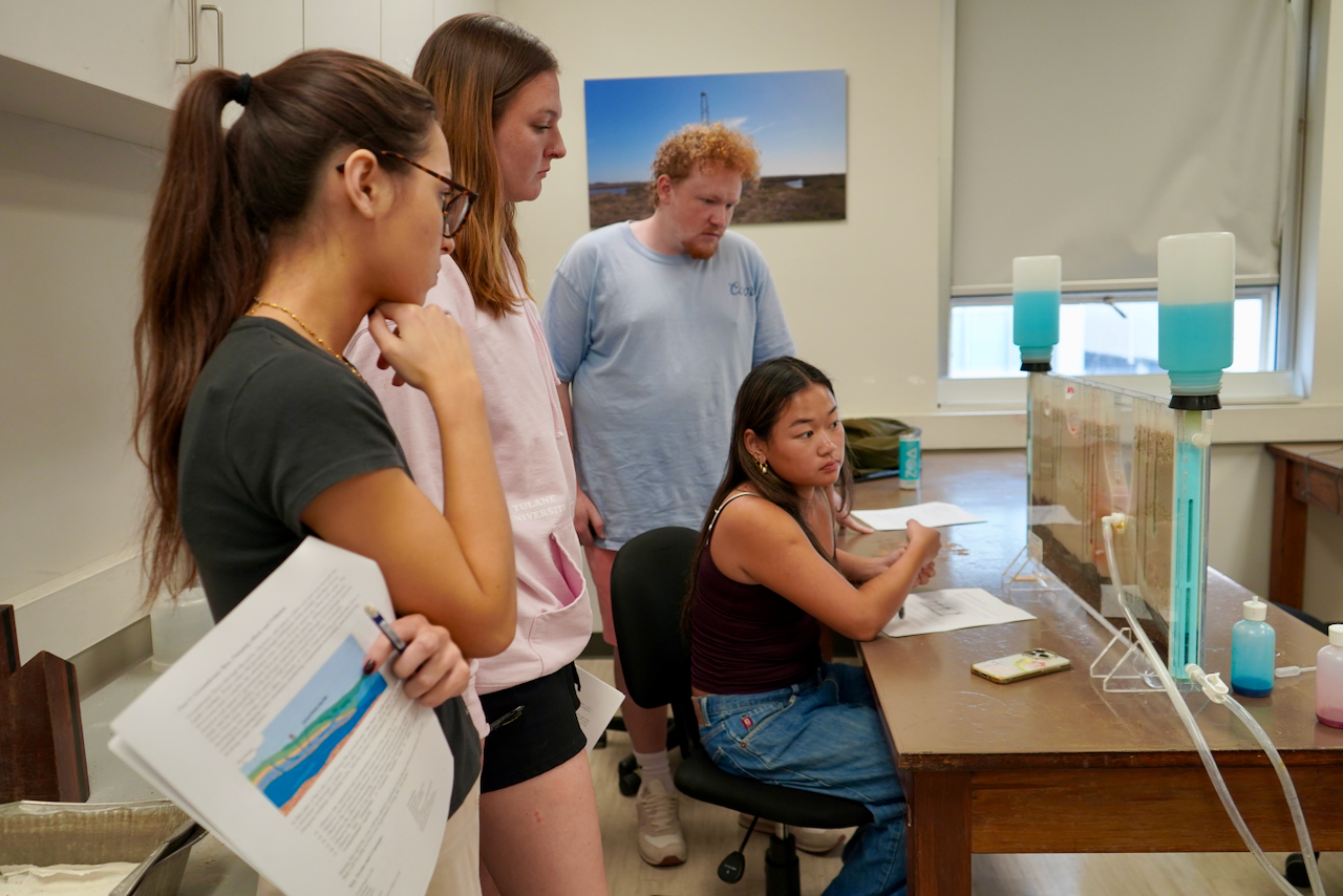 Four students gather around a desk in a brightly lit classroom for an experiment.