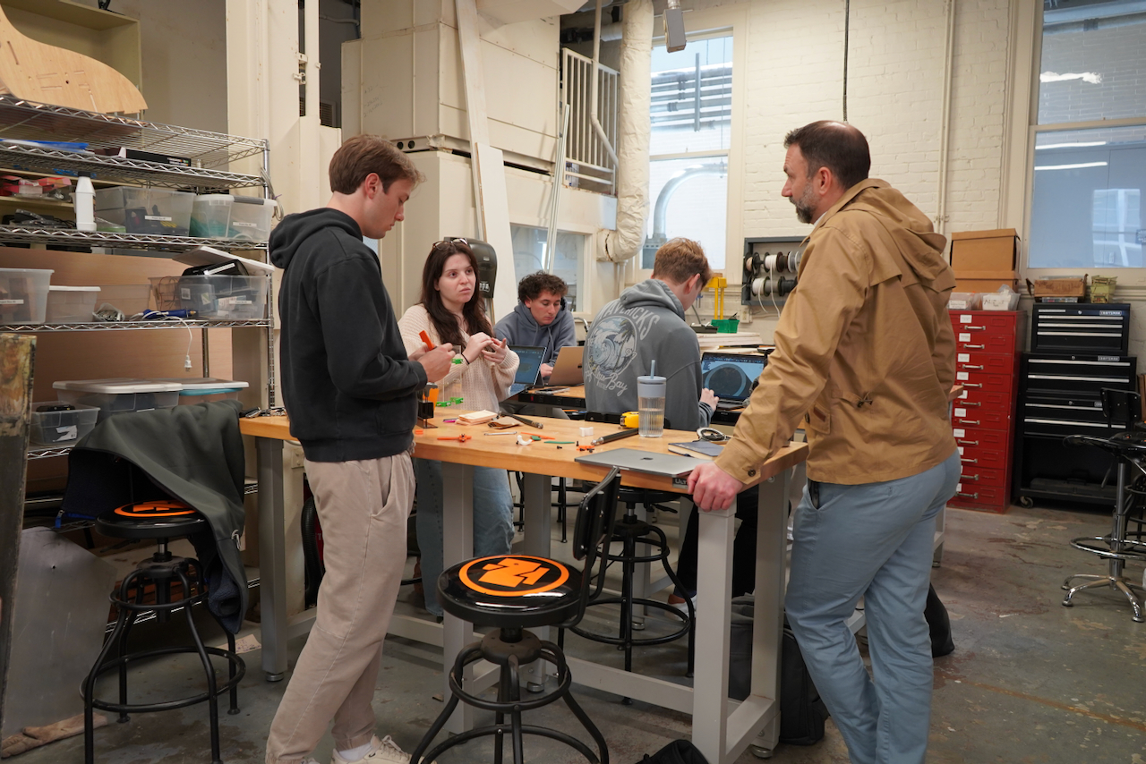 Photograph of students collaborating around a workbench in a cluttered workshop.