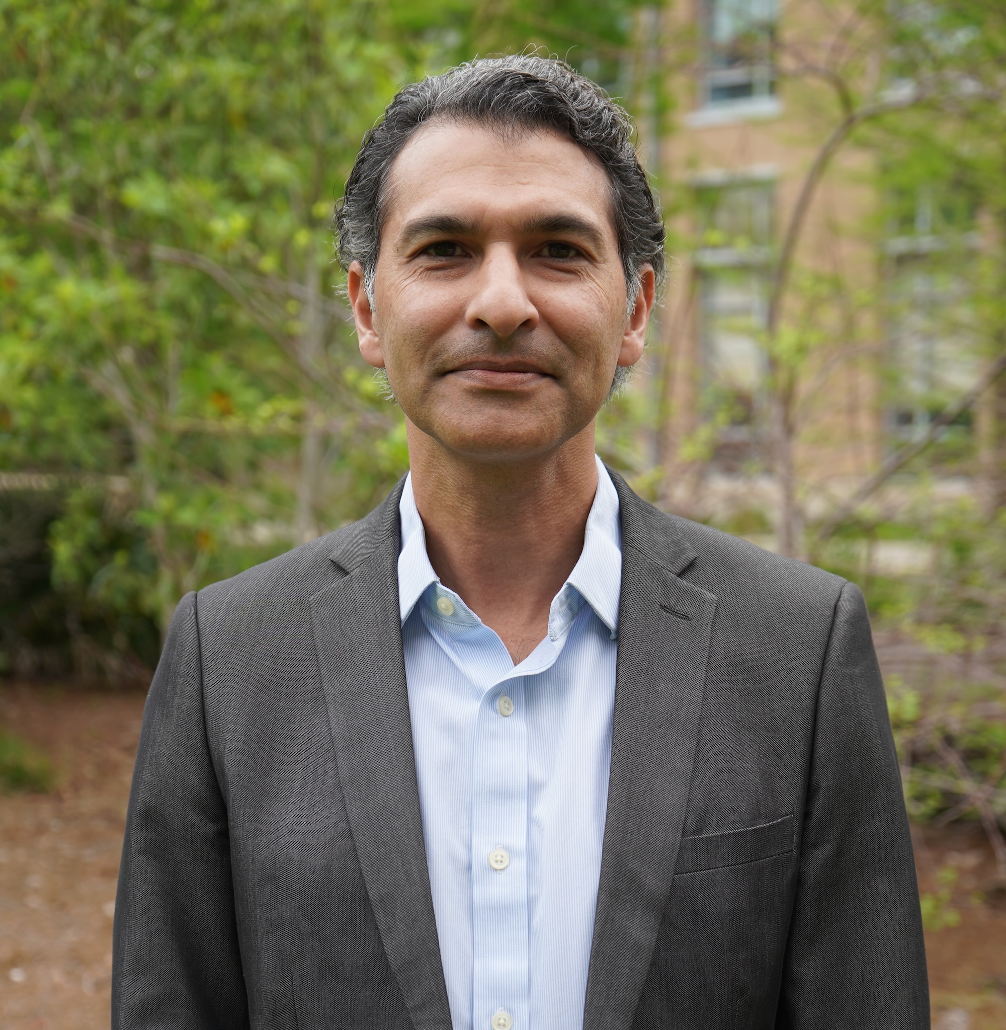 Photograph of a middle-aged man in a suit jacket and light blue shirt outdoors.