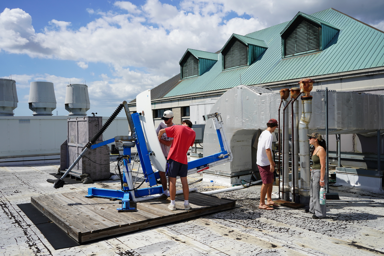 Photo of four students working on a solar dish on a rooftop.