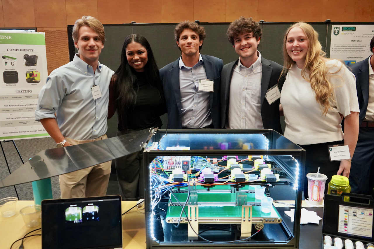Photograph of five smiling students posing behind a lighted technical display.