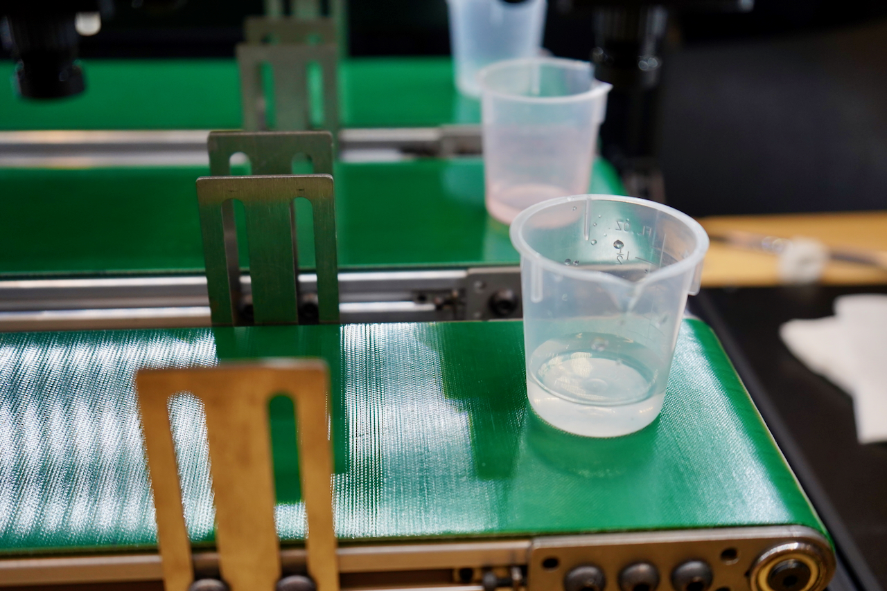 Photograph of small plastic cups on a green conveyor belt.
