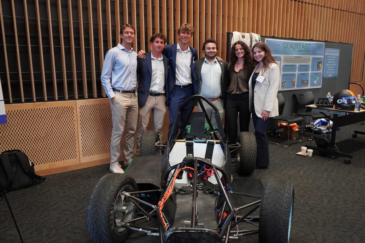 Photograph of six smiling students standing behind a racing car.