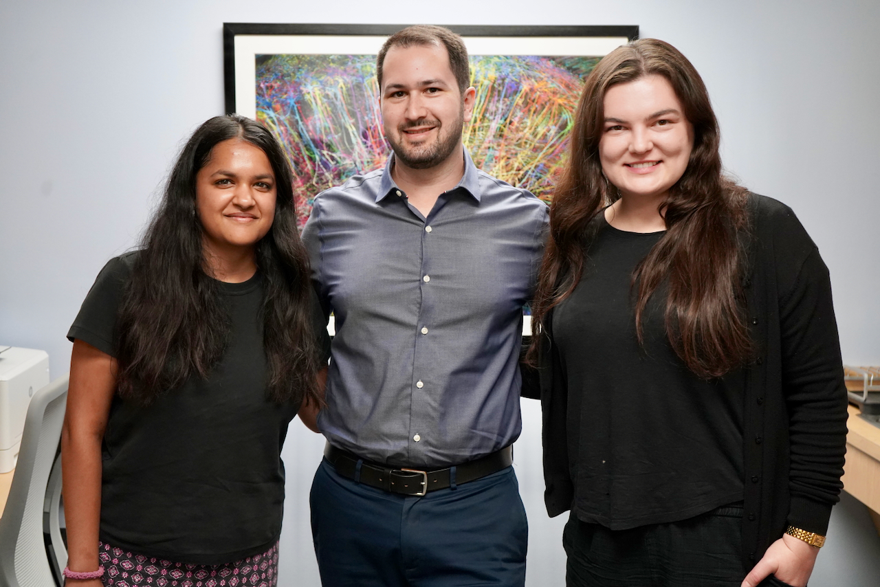 Photograph of three smiling colleagues standing in an office.