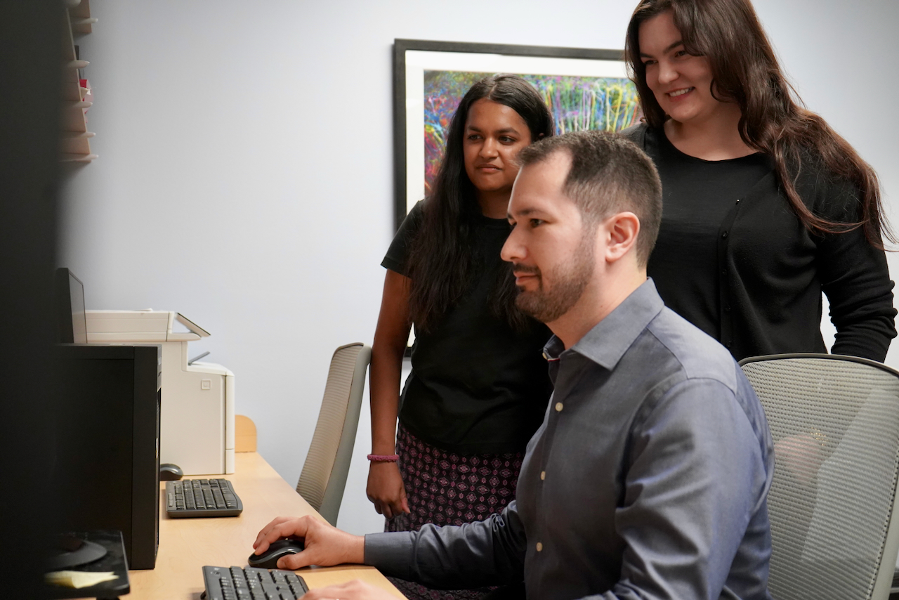 Photograph of three people looking at a computer in an office.