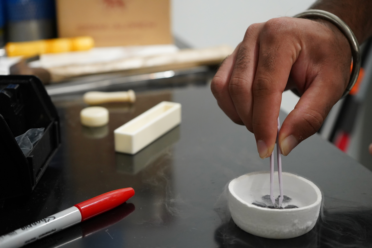 Hand using tweezers to pick something out of a small white bowl