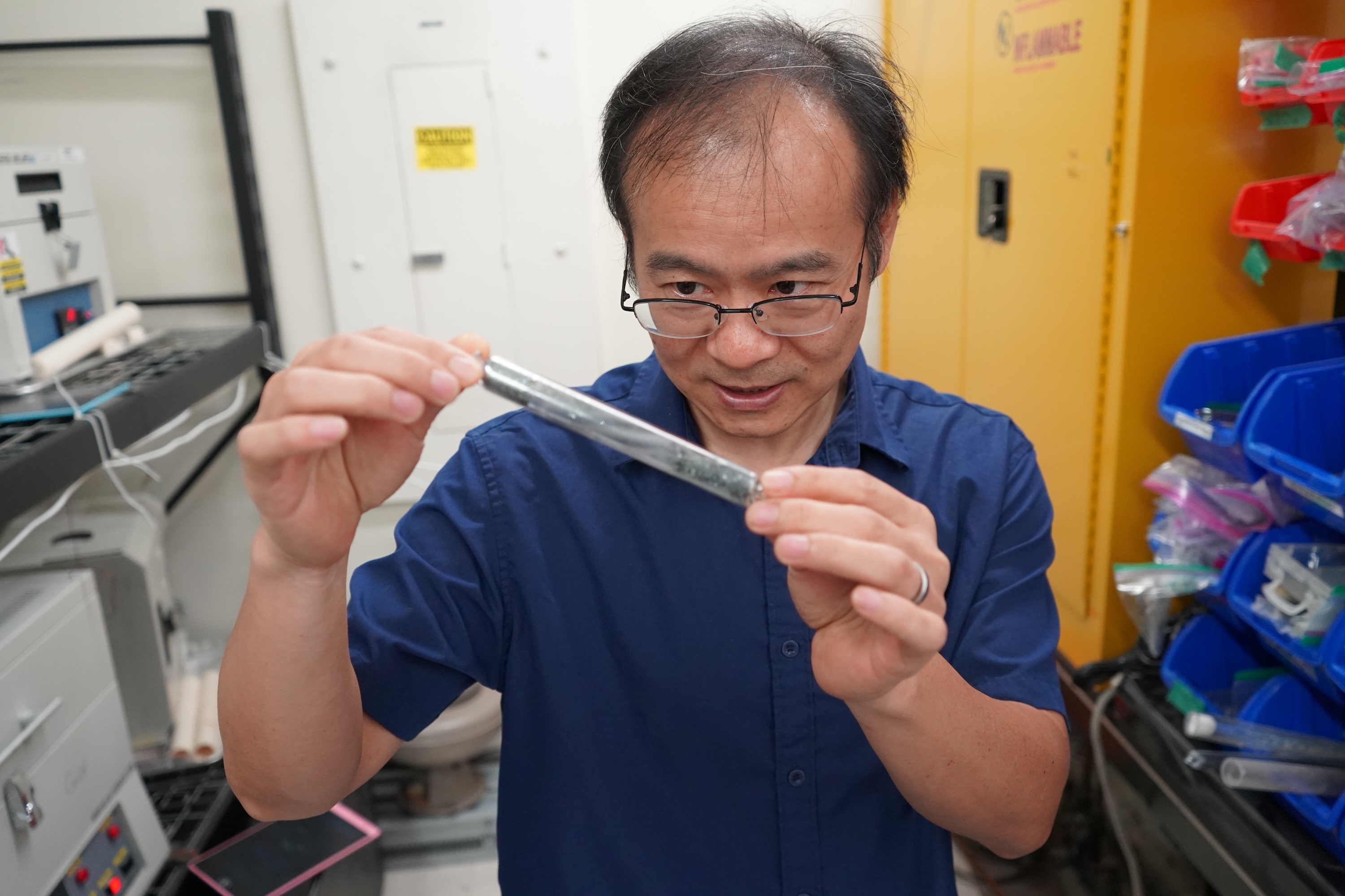 Photograph of a scientist holding a metal cylinder in a lab.