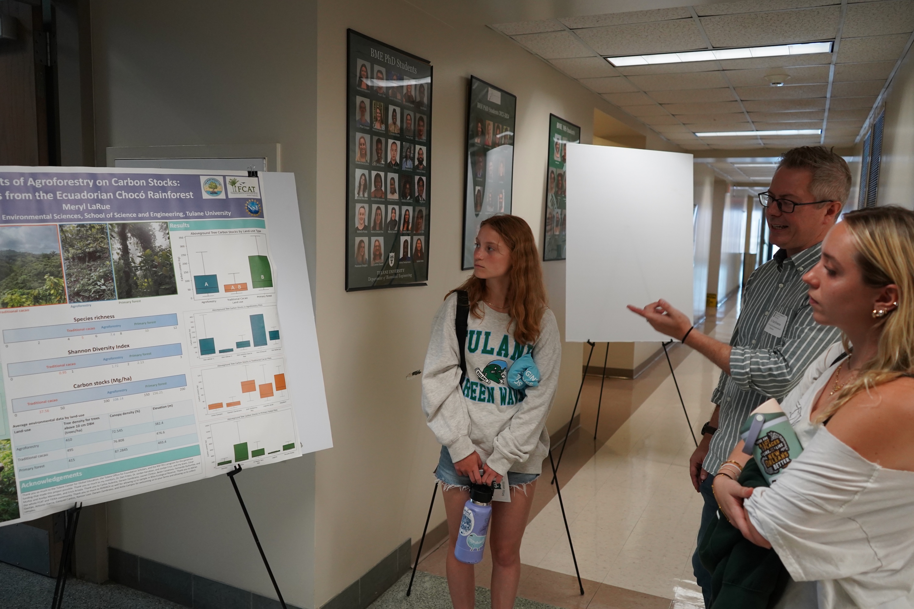 Photo of three people looking at a poster in a hallway.