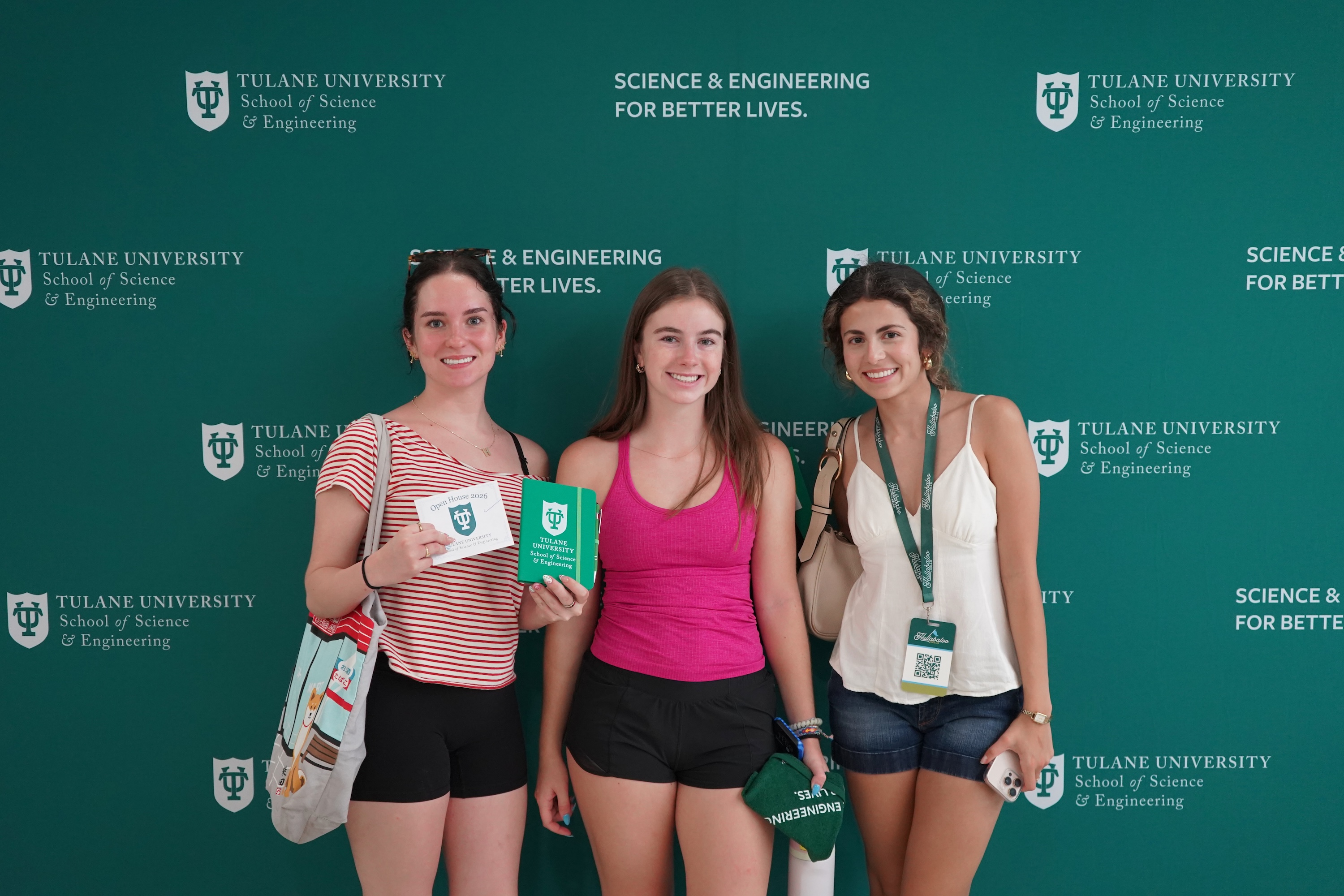 Photograph of three young women smiling in front of a green Tulane University backdrop.