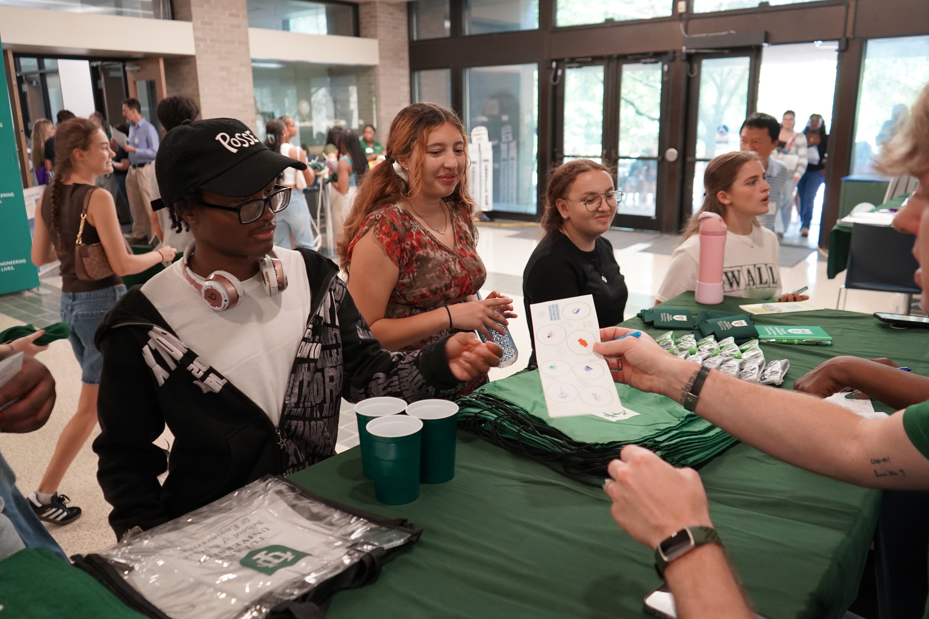 Students interacting at an information table in a busy hallway.