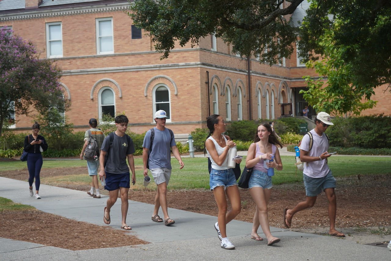 Photograph of students walking on a campus path before a brick building.