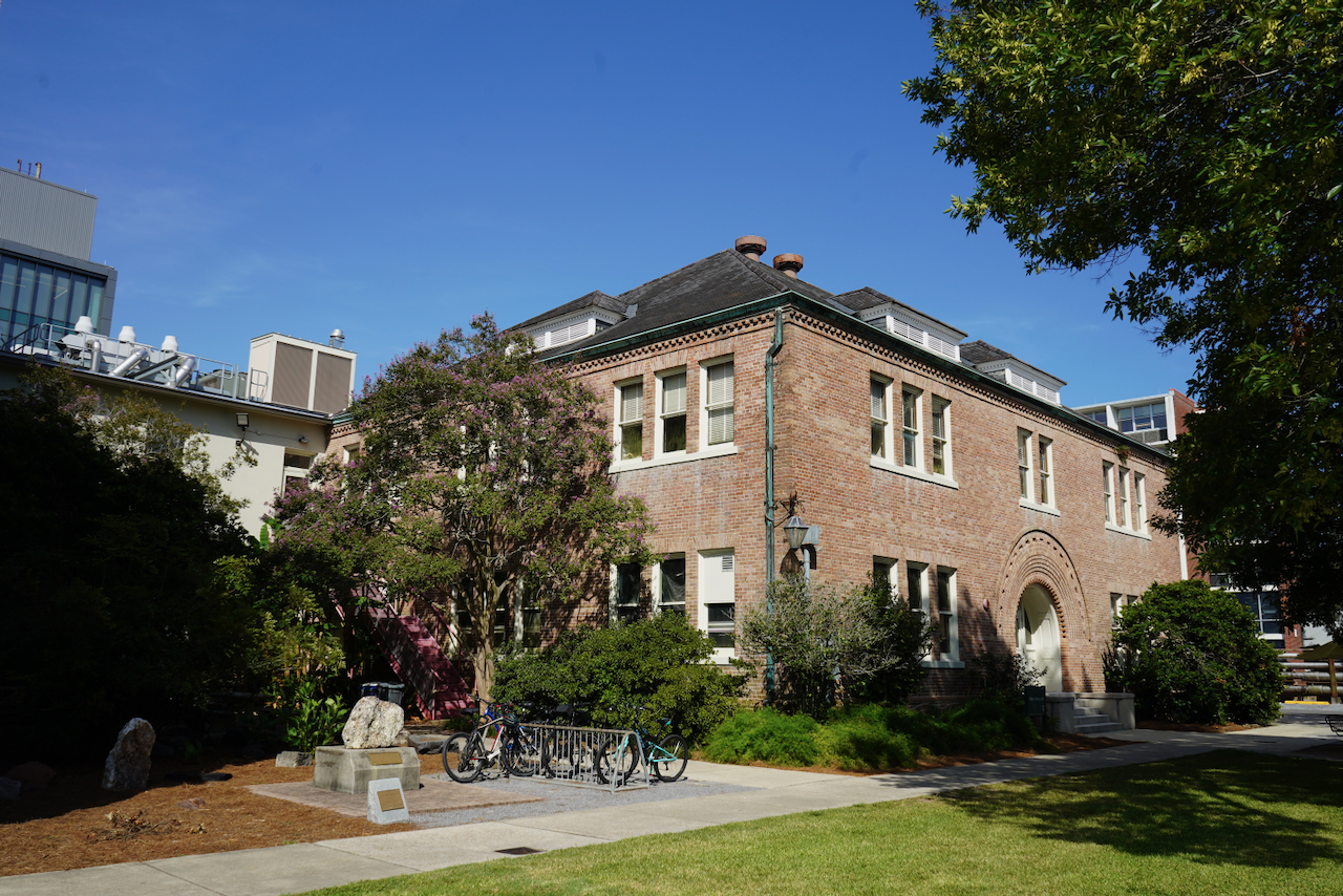 Photograph of a two-story brick building surrounded by trees under a clear blue sky.