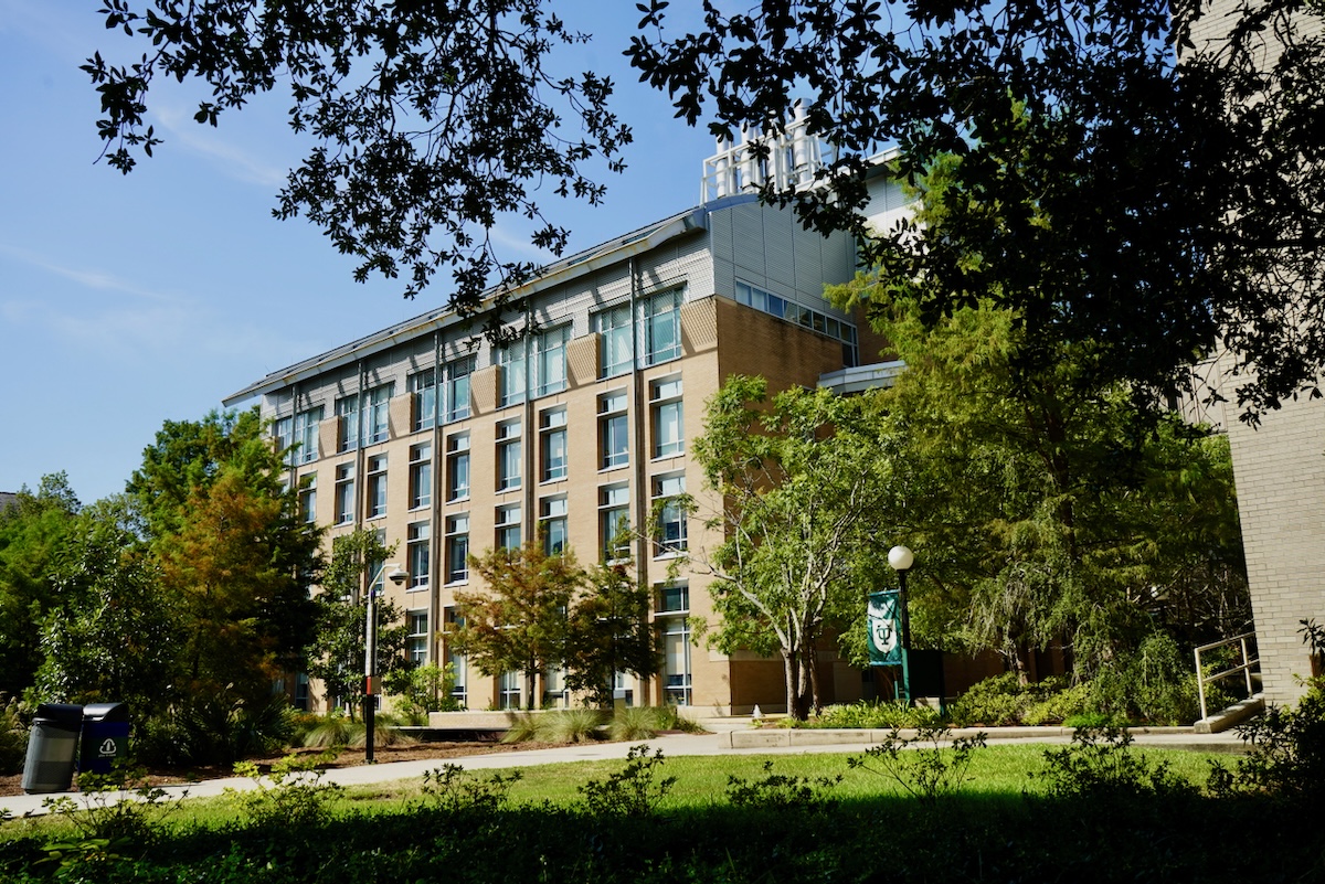 Photograph of a modern multi-story brick and glass building framed by trees.