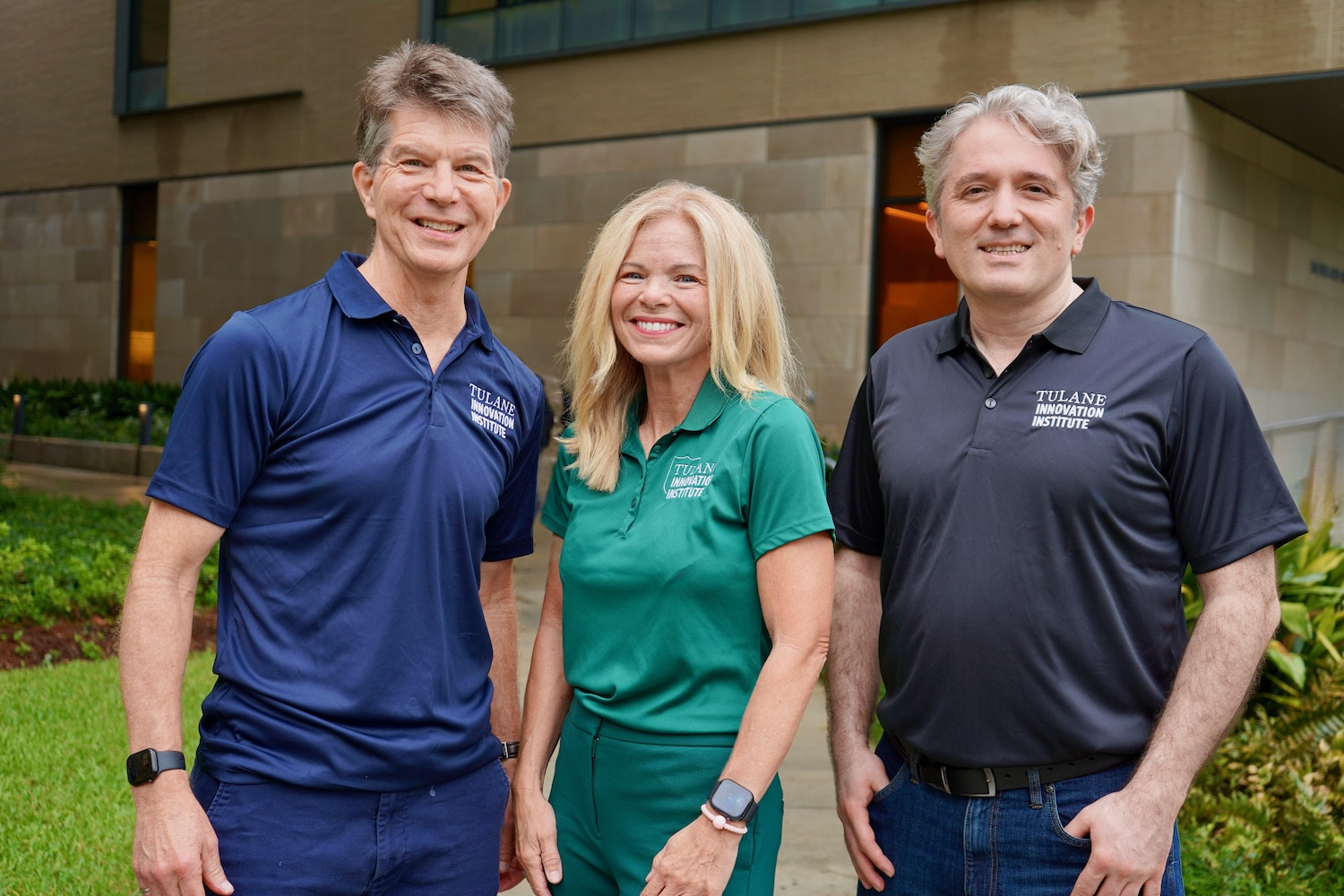 Photograph of three people smiling outdoors in front of a building.