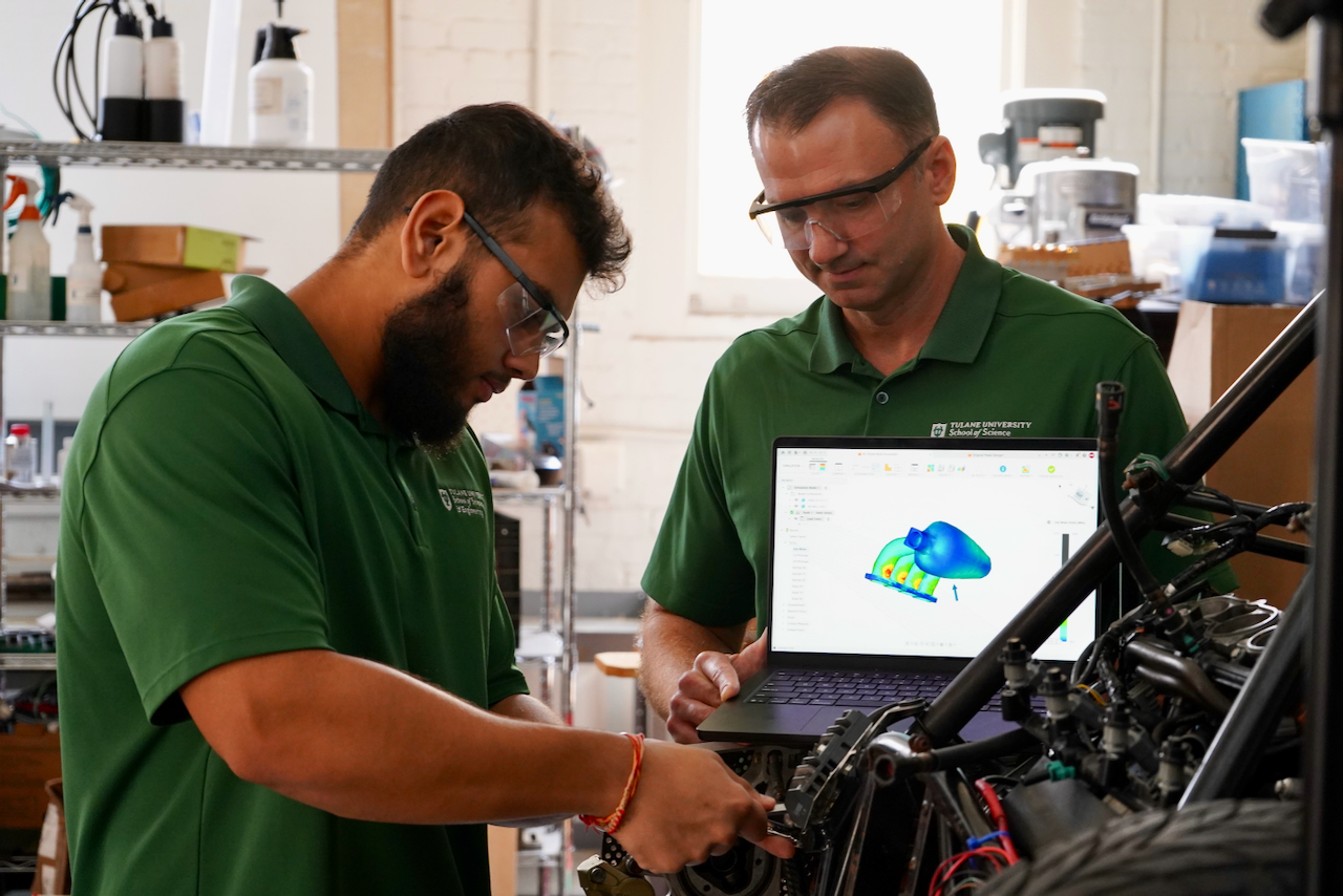 Photo of two engineers wearing green shirts working on a go-kart in a workshop.