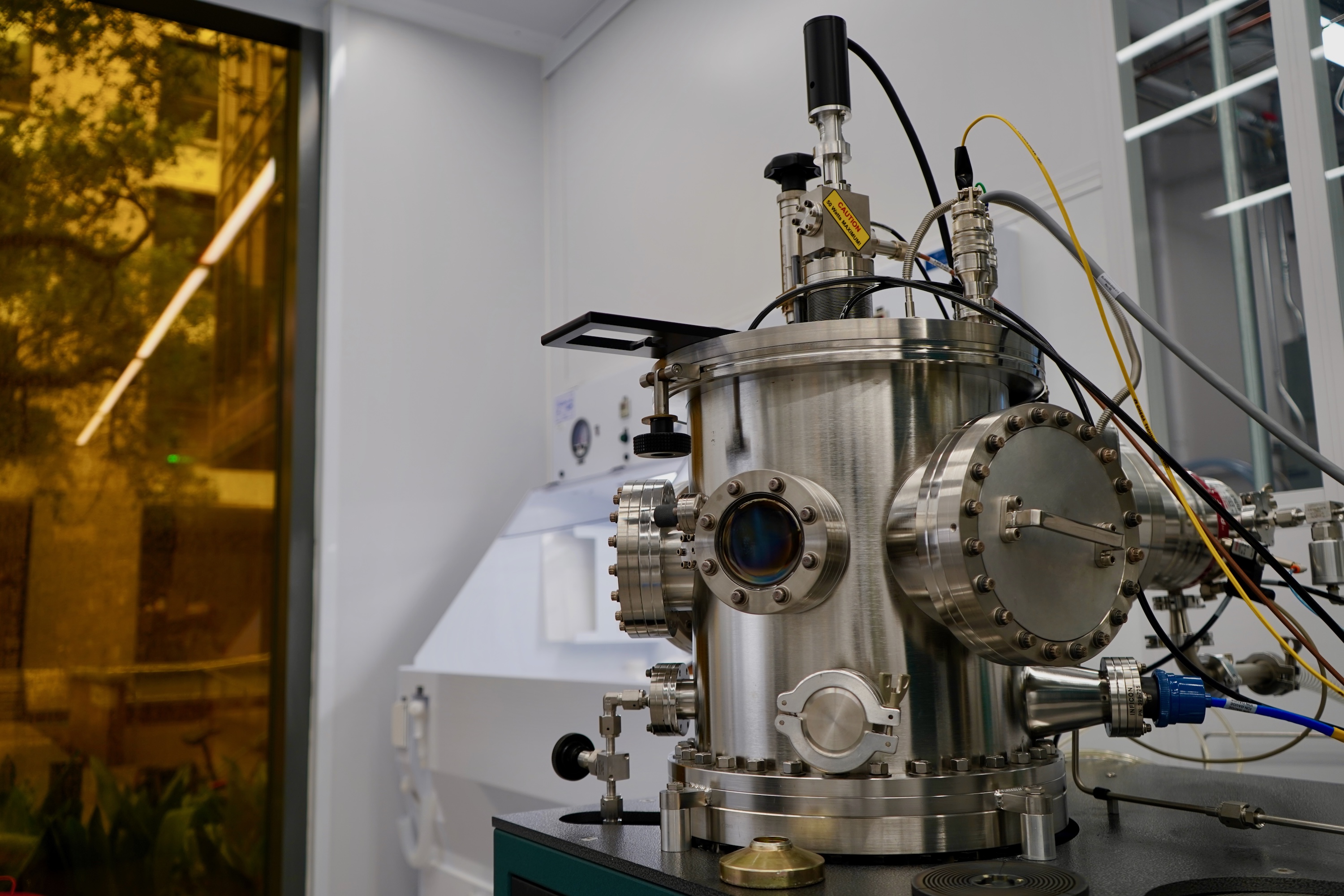 A photograph of a large, complex metal vacuum chamber with viewports, gauges, and wiring in a lab.