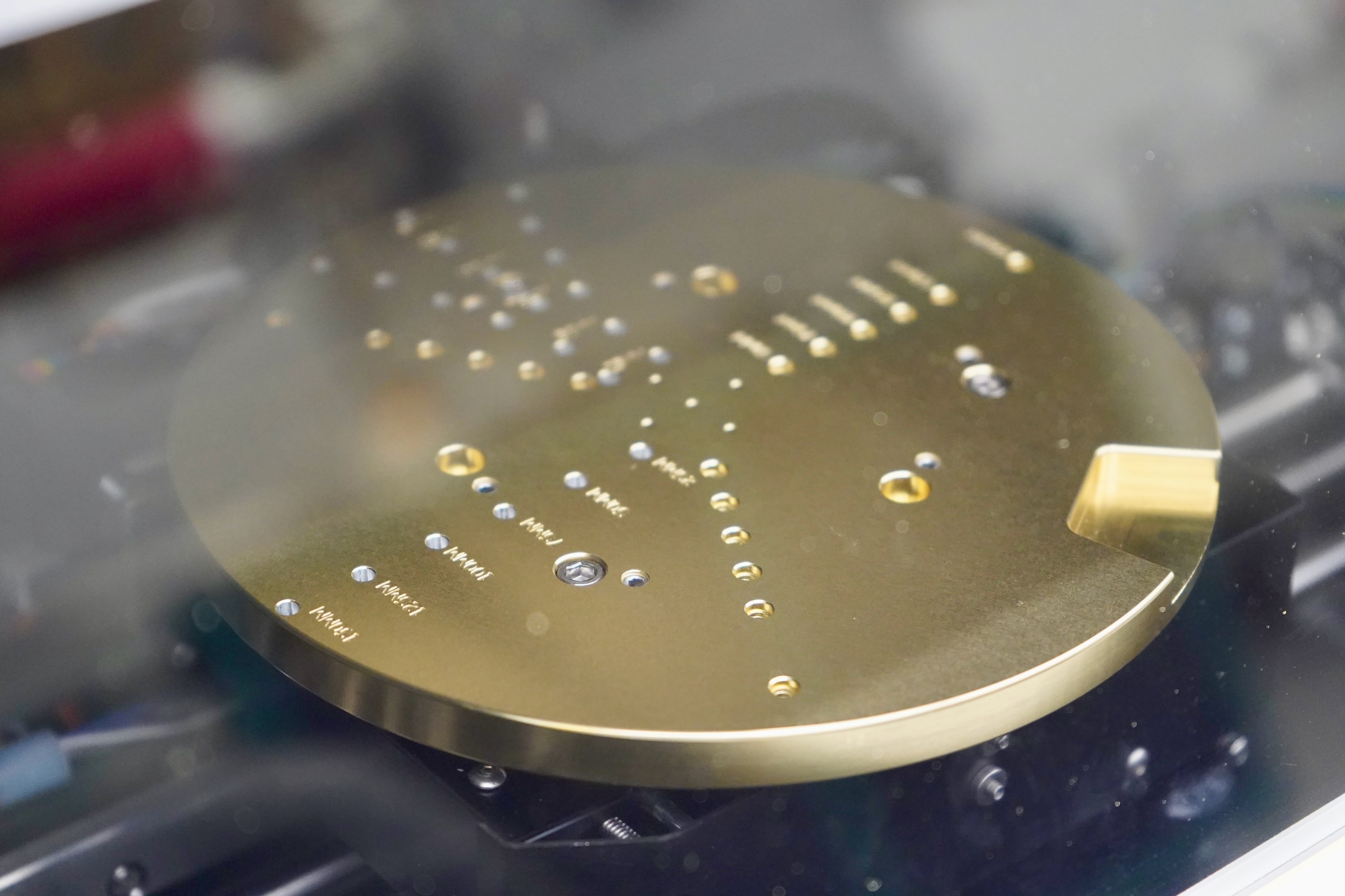 Photograph of a brass disc with micro-machined holes on a robotic arm.