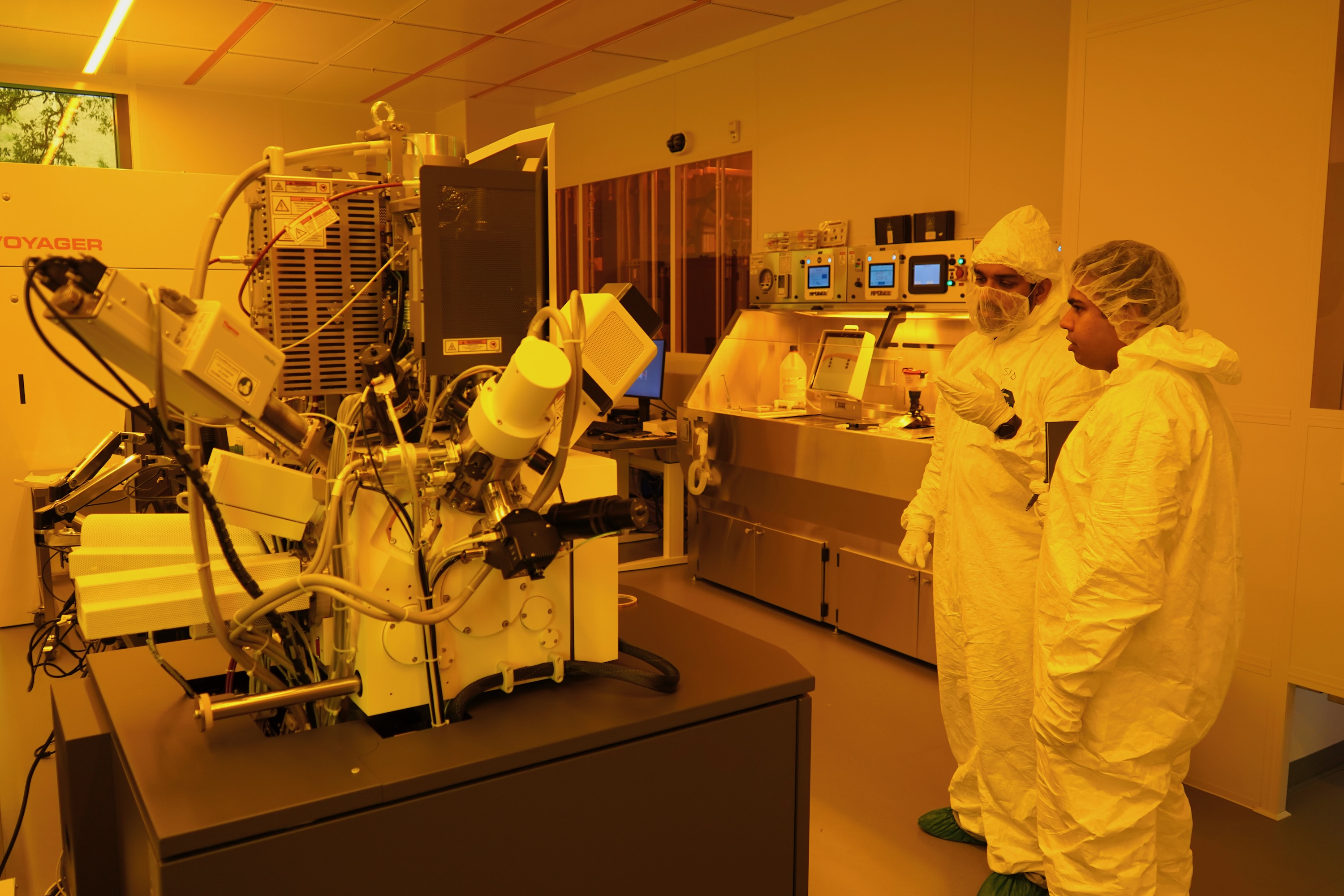 Two technicians in cleanroom suits examine laboratory equipment.