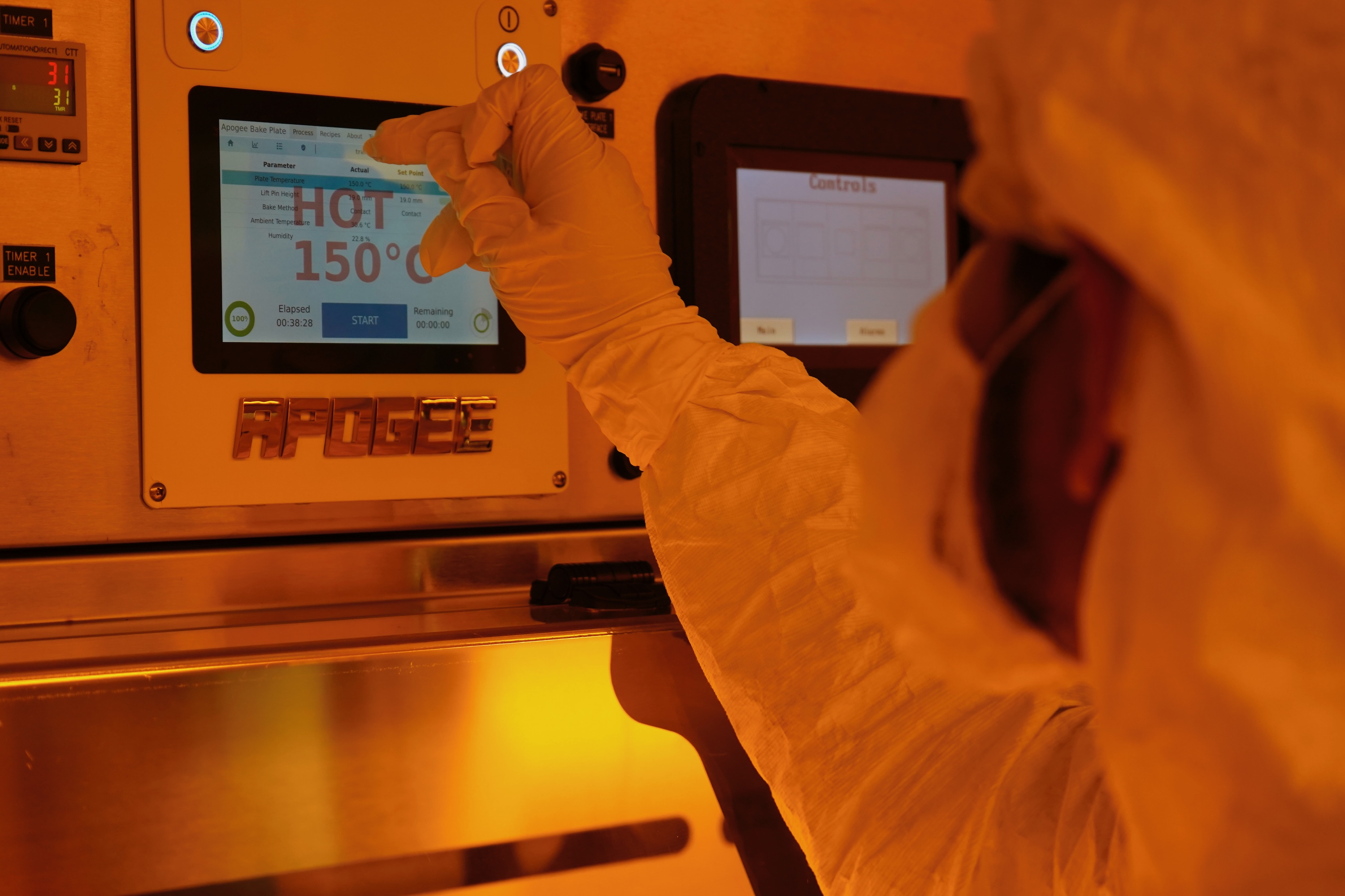 Photograph of a worker in a cleanroom adjusting a digital control panel with a stylus.