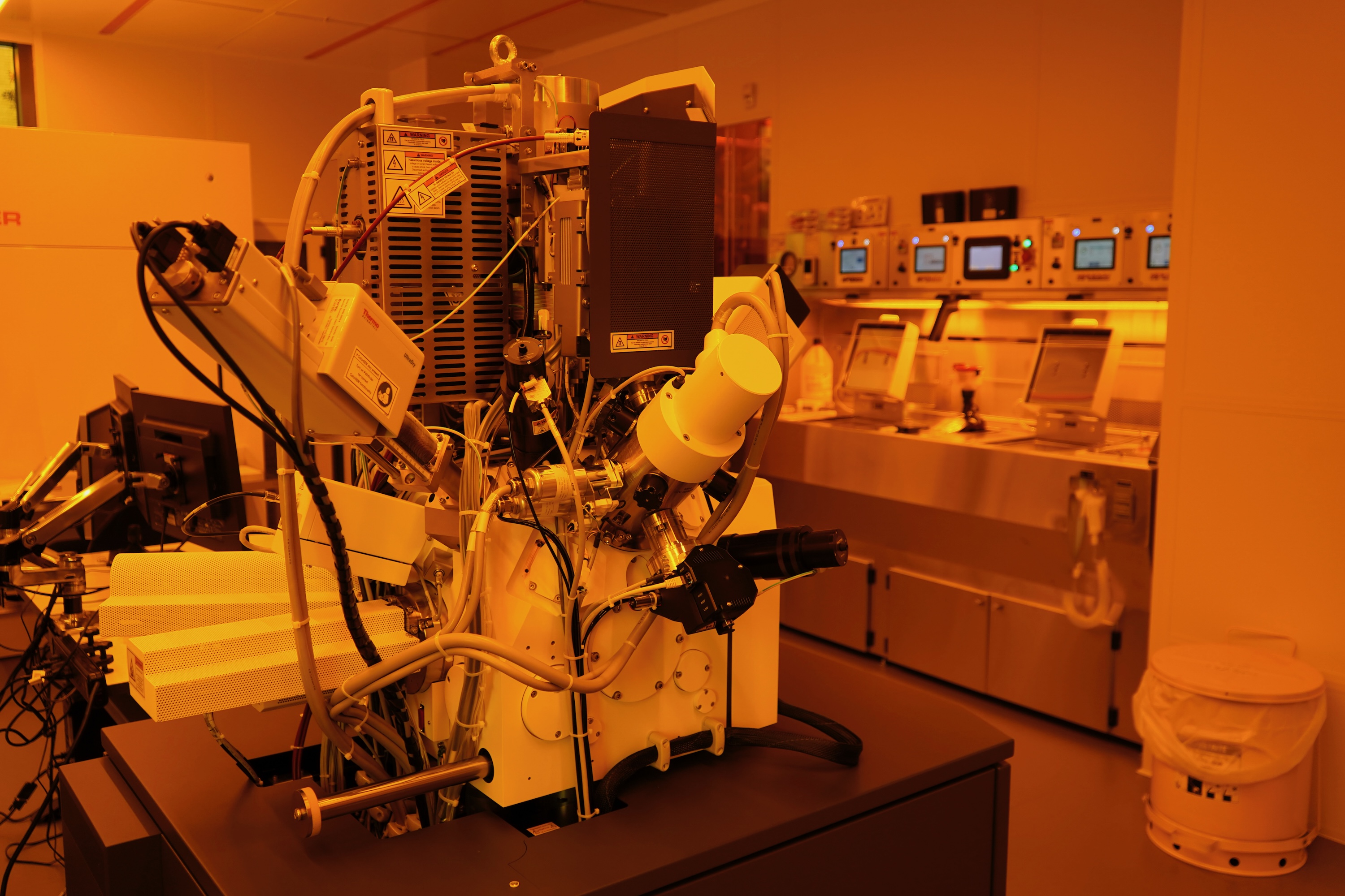Photograph of a complex laboratory machine bathed in amber light in a cleanroom.