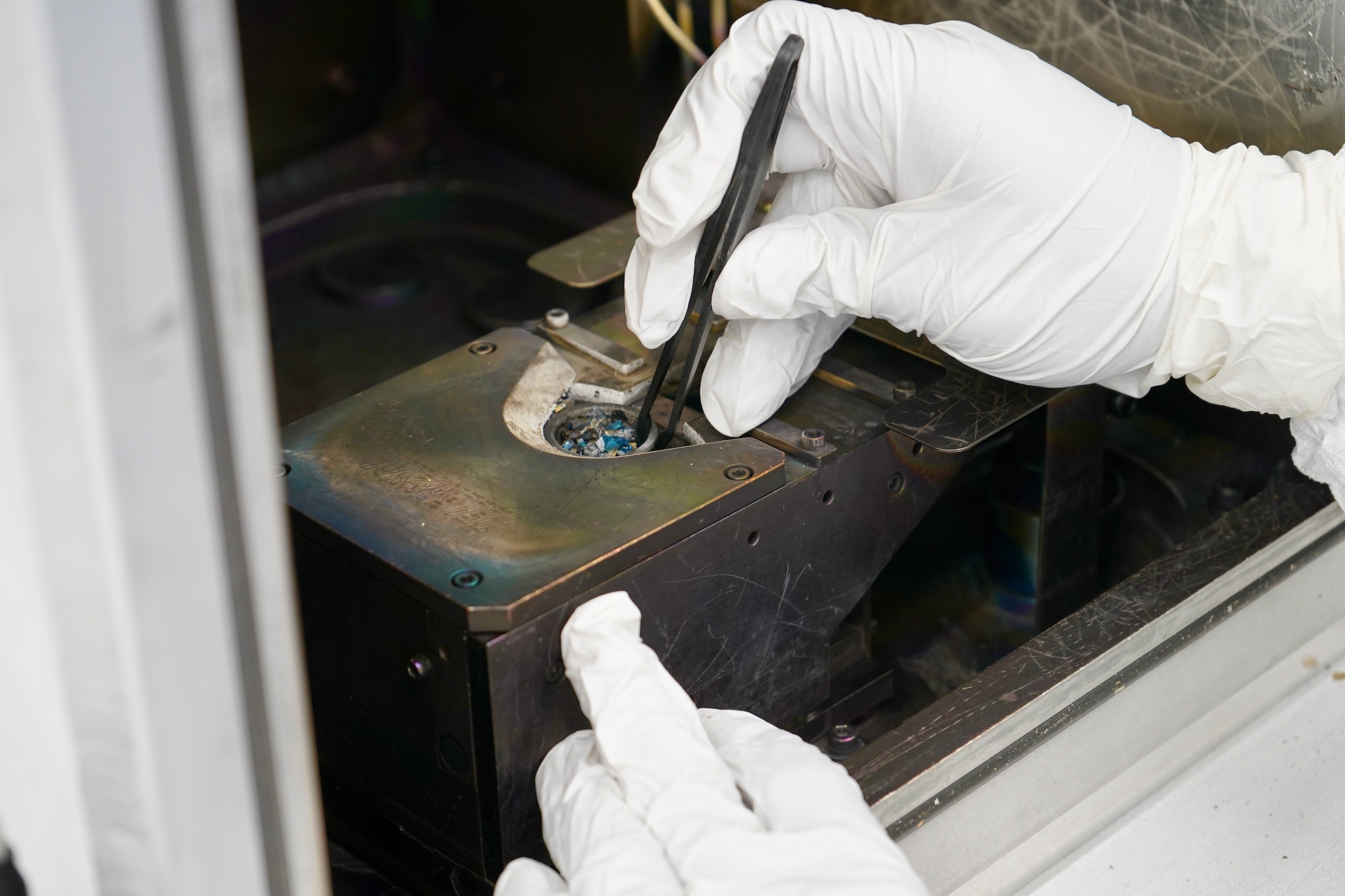 A gloved hand uses tweezers to precisely assemble a complex mechanical device.
