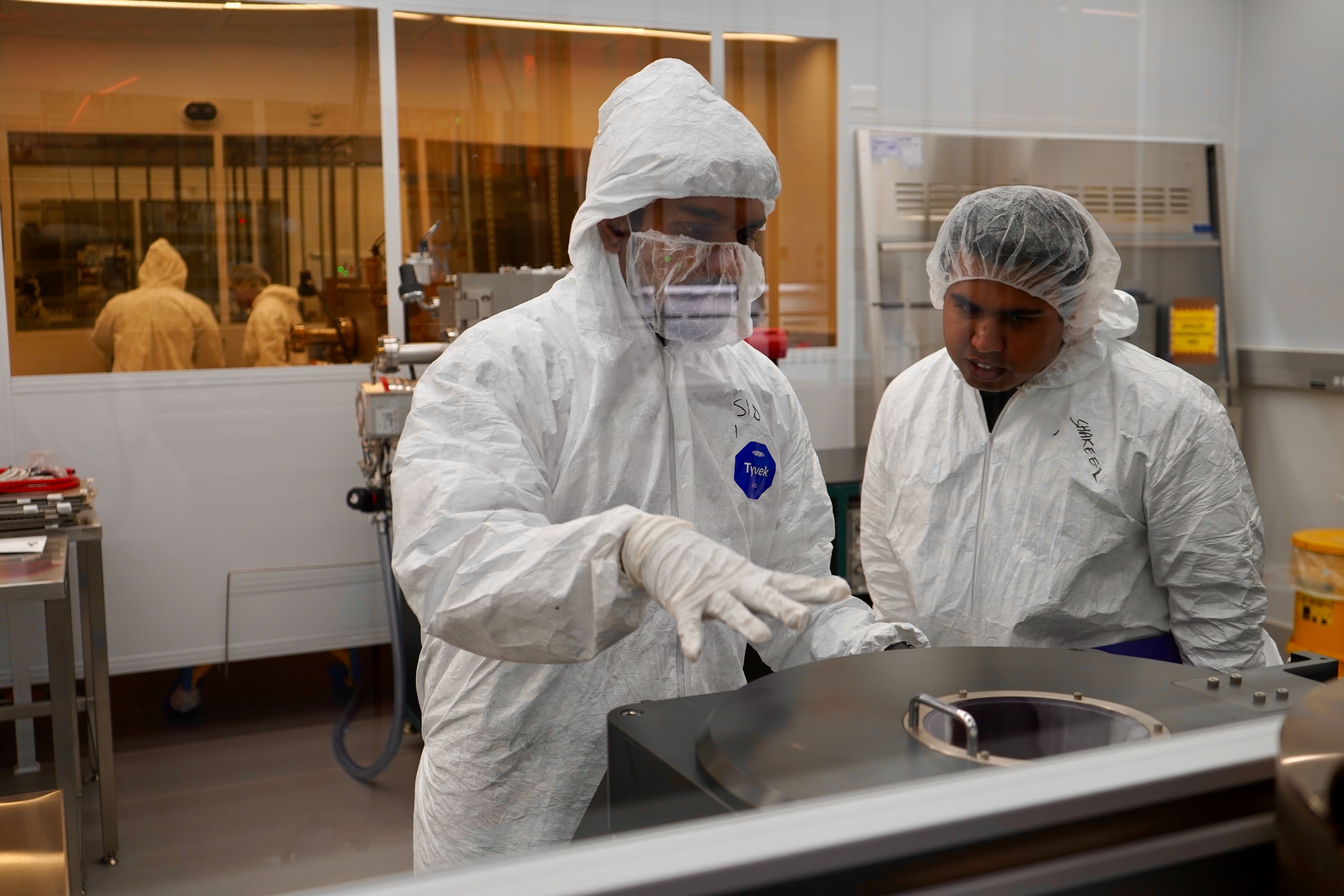 Two workers in white protective suits and hairnets working in a cleanroom.