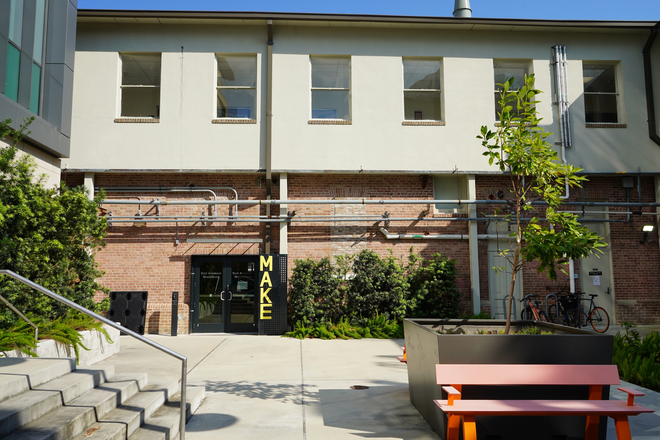 A photograph of an urban courtyard featuring a pink bench and a brick building facade.