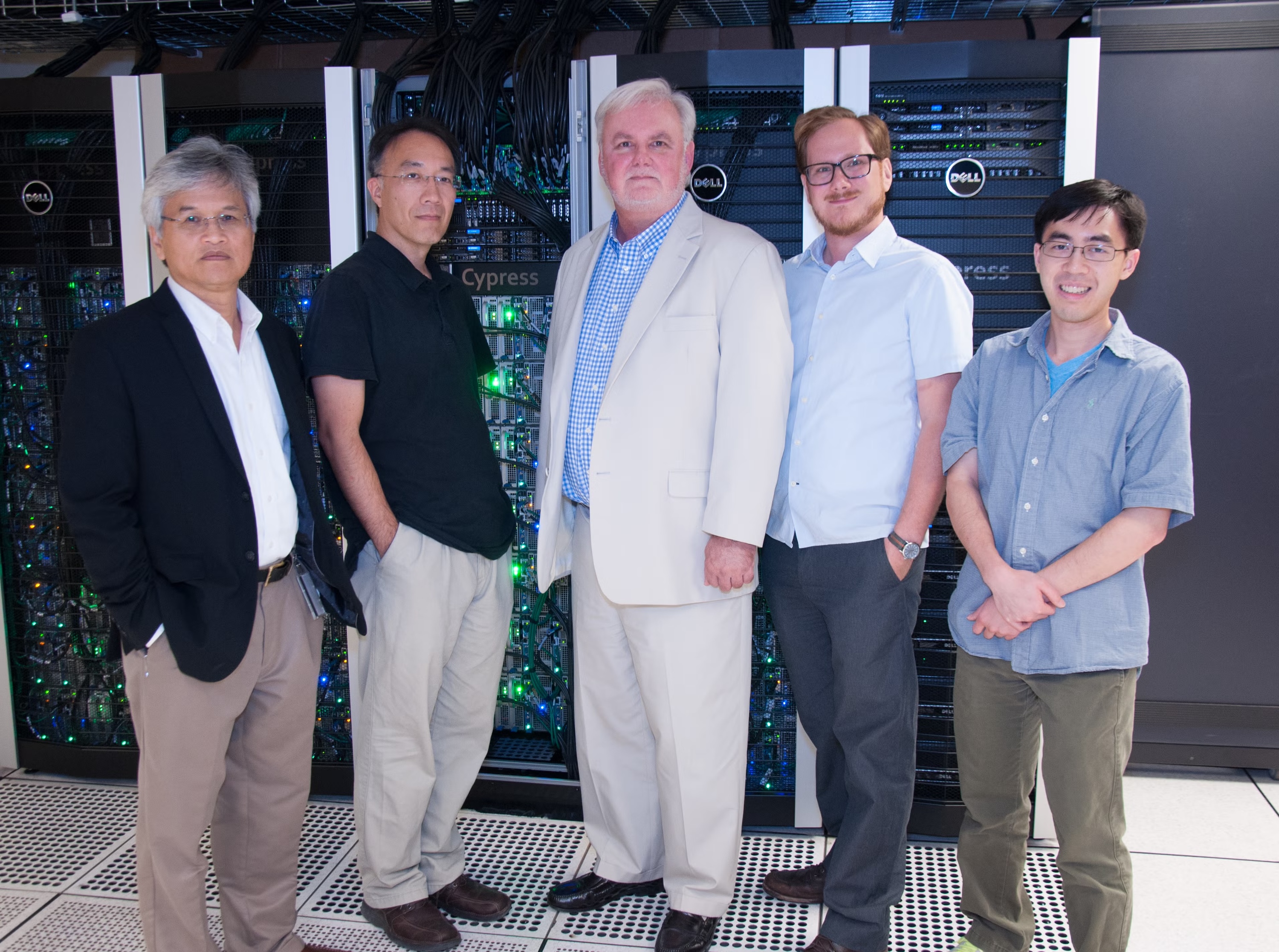 Photograph of five men standing in a row in front of server racks.
