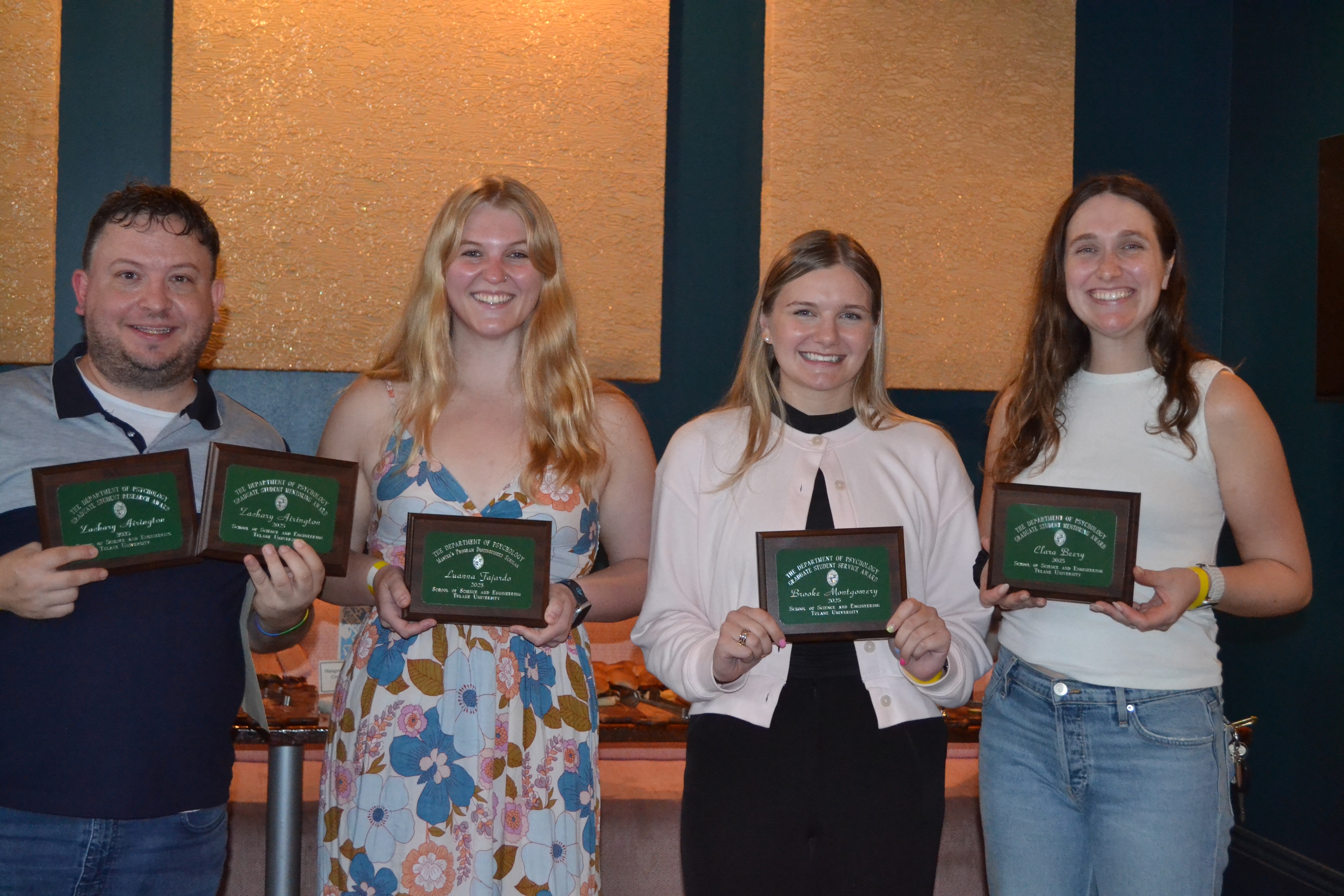 Photograph of four smiling colleagues holding award plaques in a decorated room.