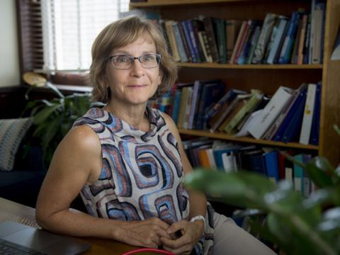 Photograph of a smiling woman with glasses seated in an office with a bookshelf.