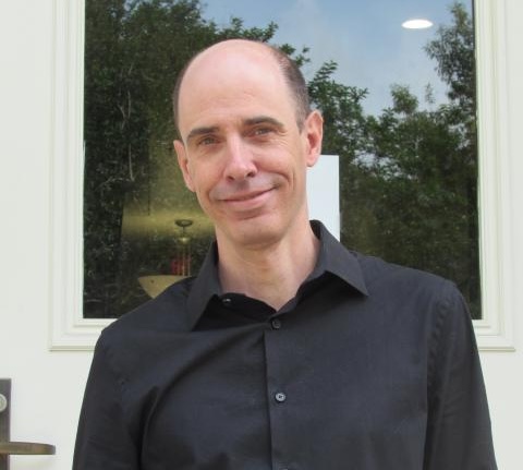 Photograph of a middle-aged bald man in a black button-down shirt smiling.