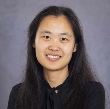 Photograph of a smiling Asian woman with long dark hair against a grey background.