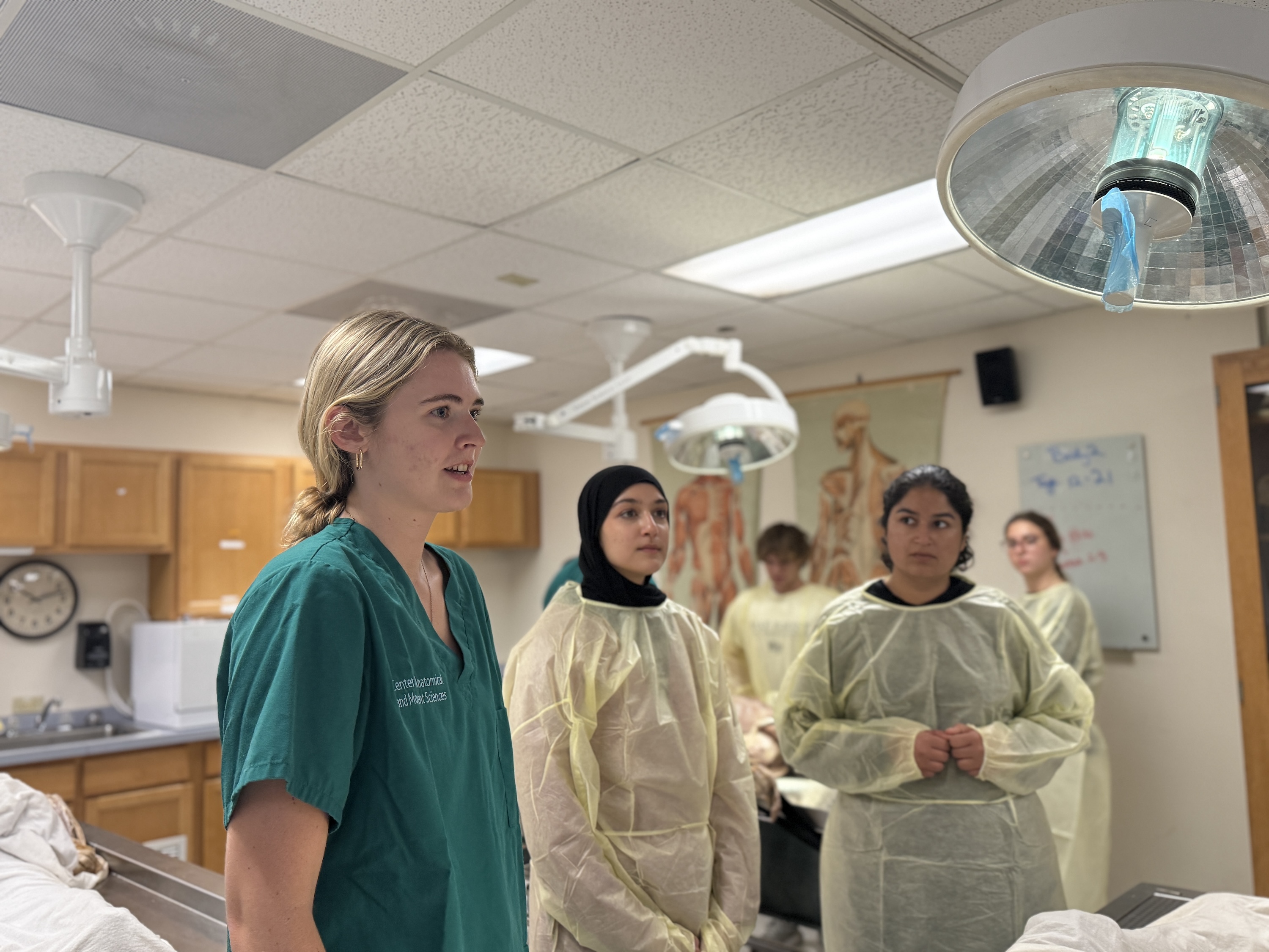 Photograph of medical students in a lab, with one in green scrubs speaking.