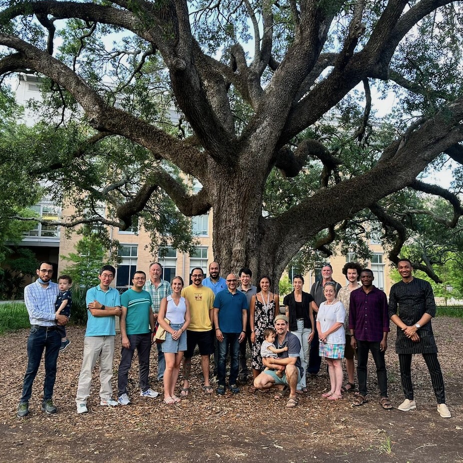 Photograph of a group standing together in front of a large tree.