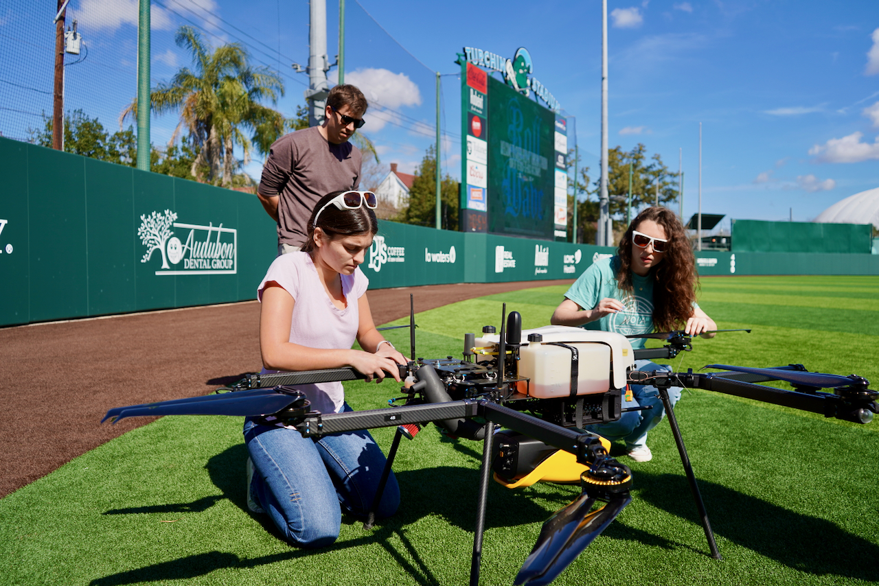 Photograph of three people preparing a large agricultural drone on a baseball field.