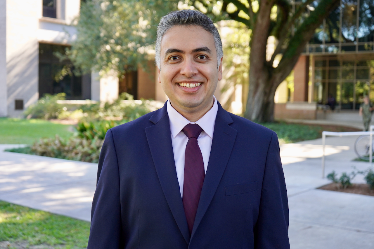 Photograph of a smiling man in a suit and tie outdoors.